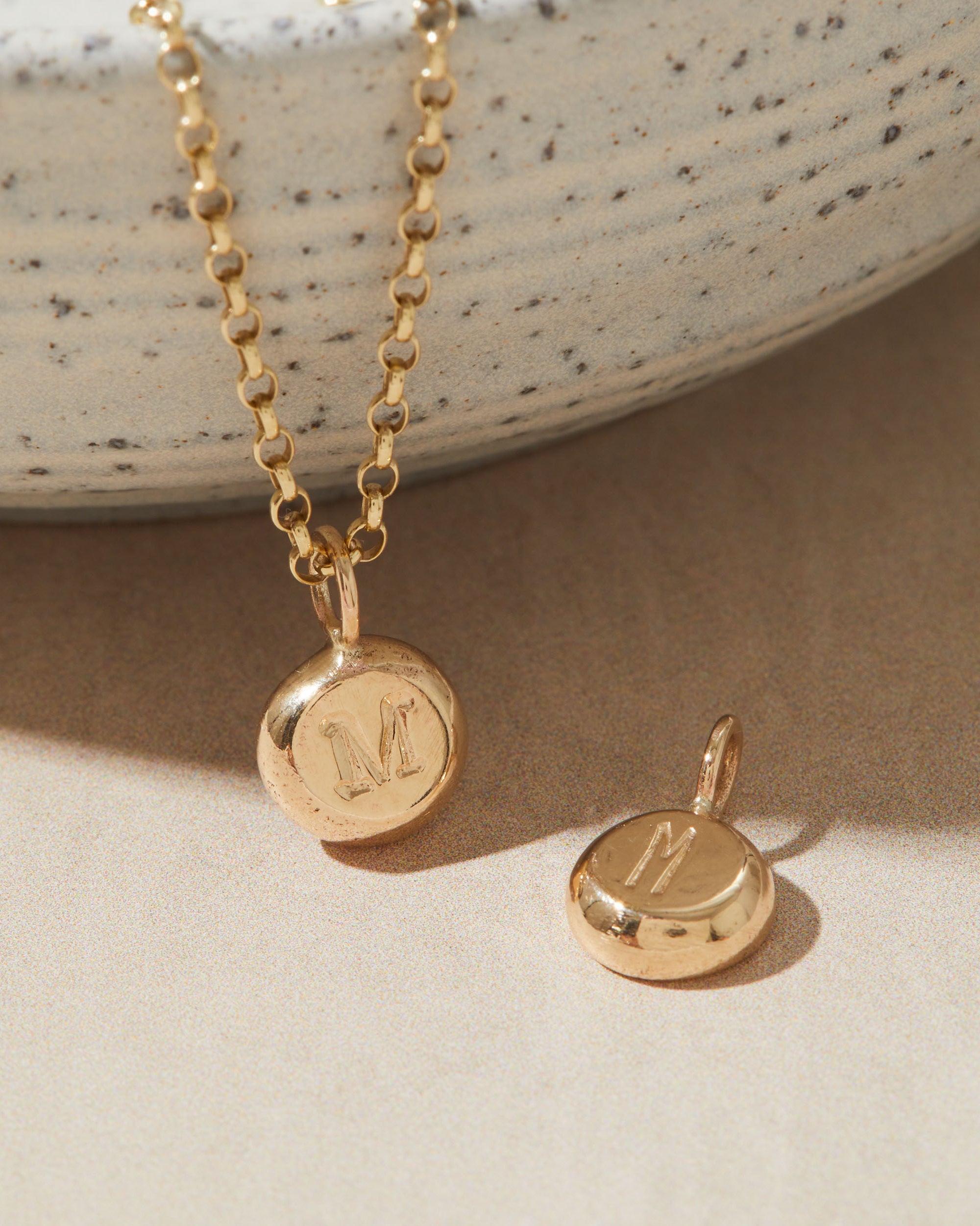 Gold necklace with a pendant featuring the letter 'M' on a neutral background