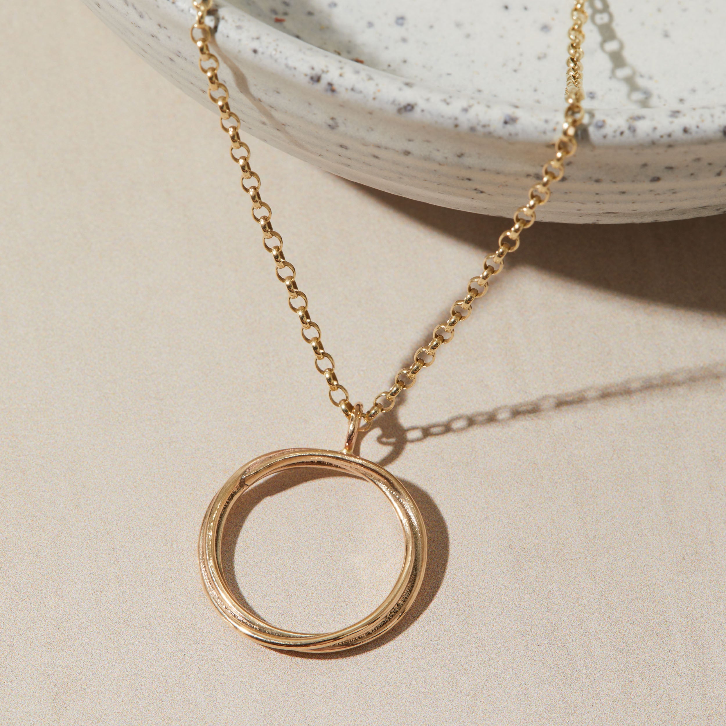 Gold necklace with a circular pendant on a beige surface