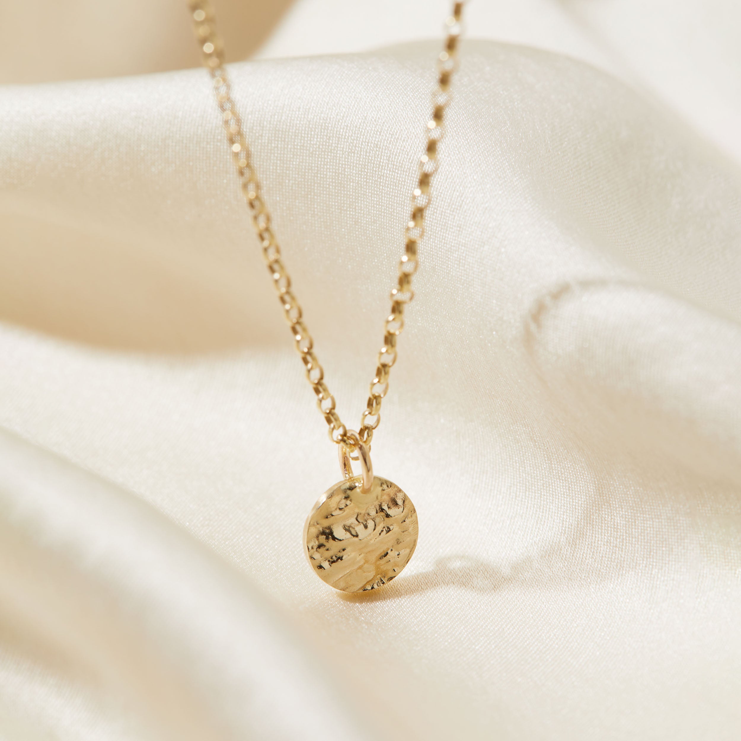 Gold necklace with a tree bark textured pendant on a soft beige background