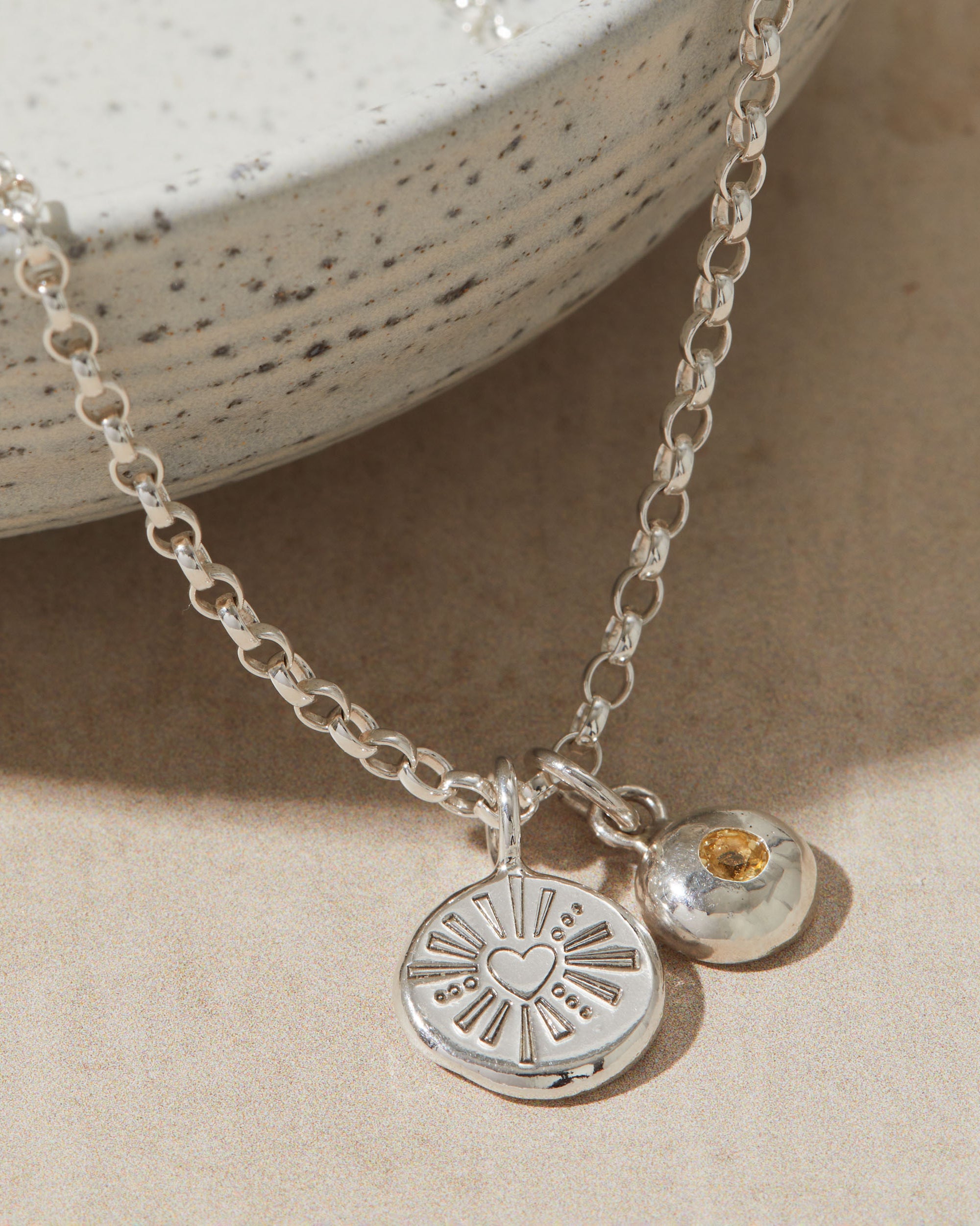 Silver necklace with a heart pendant and birthstone charm on a beige surface
