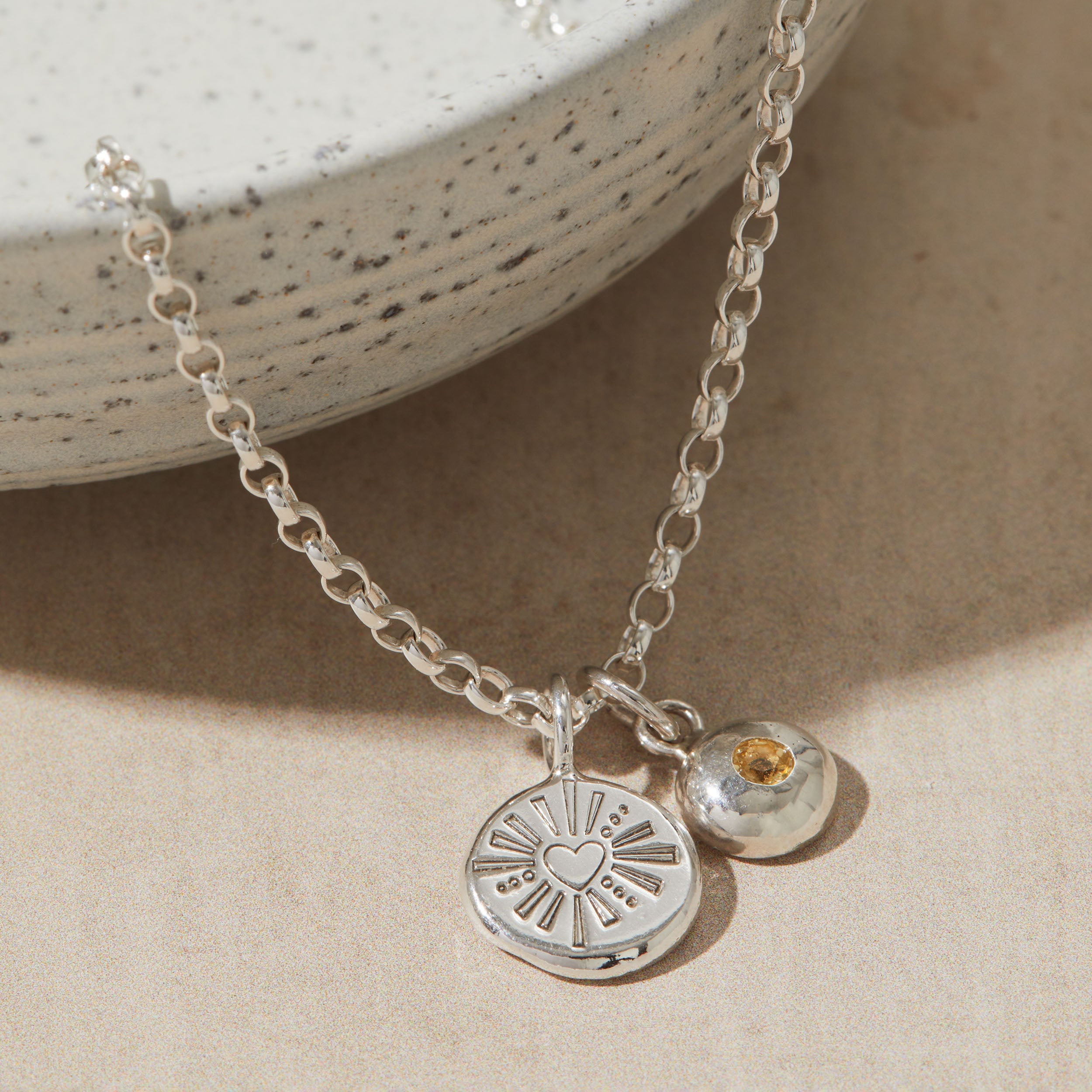 Silver necklace with a heart pendant and birthstone charm on a beige surface