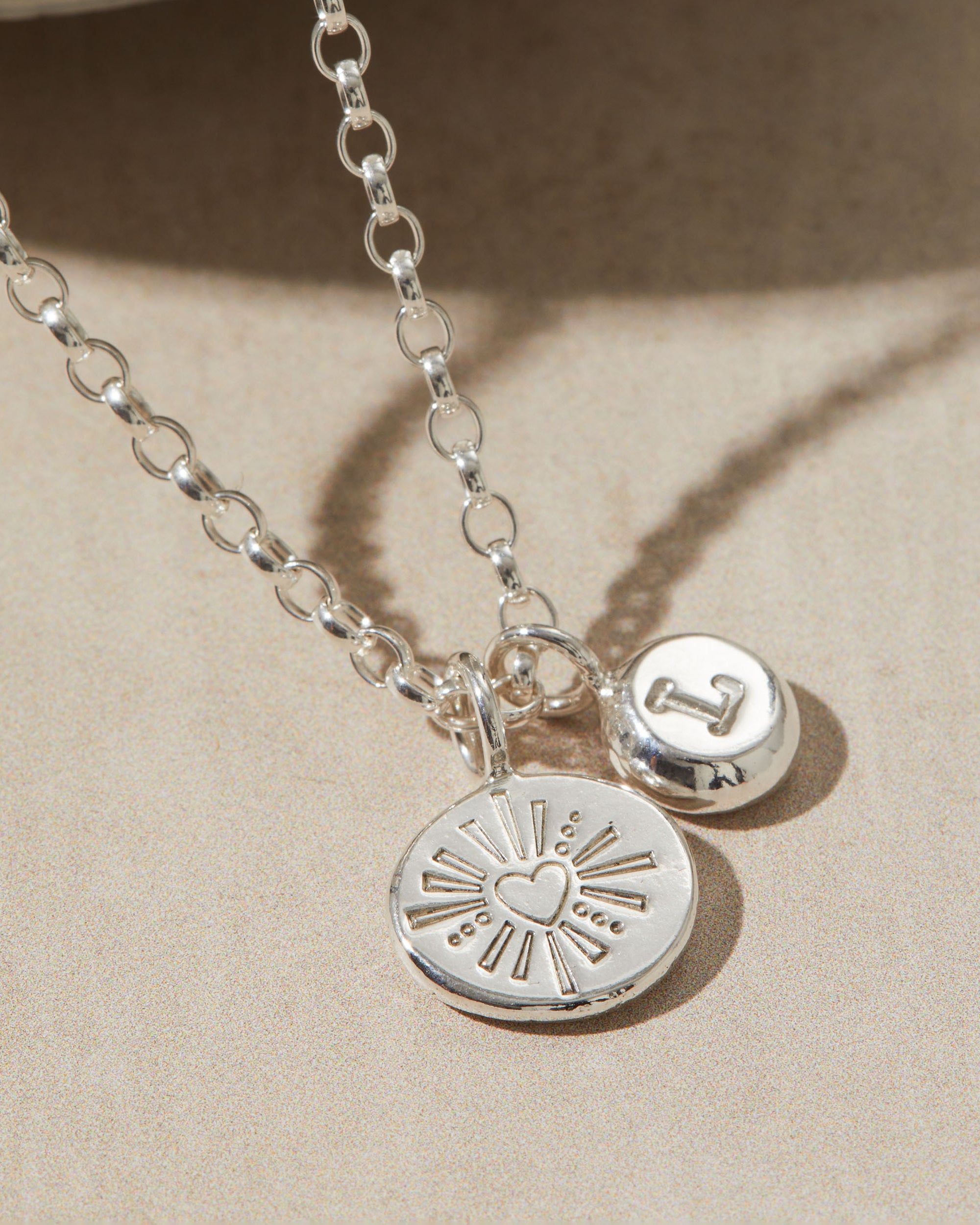 Silver necklace with heart and initial pendants on a beige background
