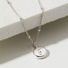 Silver necklace with a round pendant featuring the letter 'F' on a light background