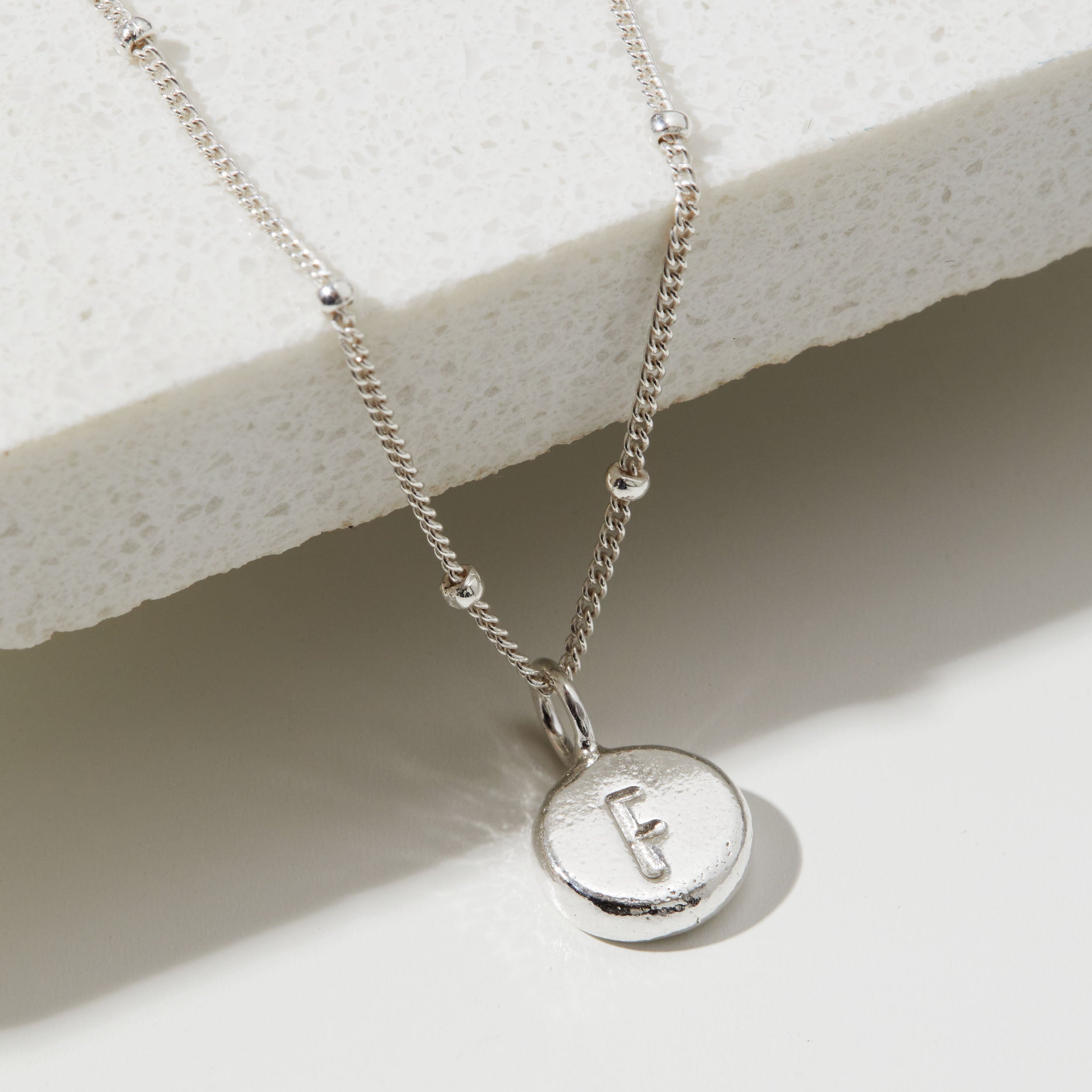 Silver necklace with a round pendant featuring the letter 'F' on a light background