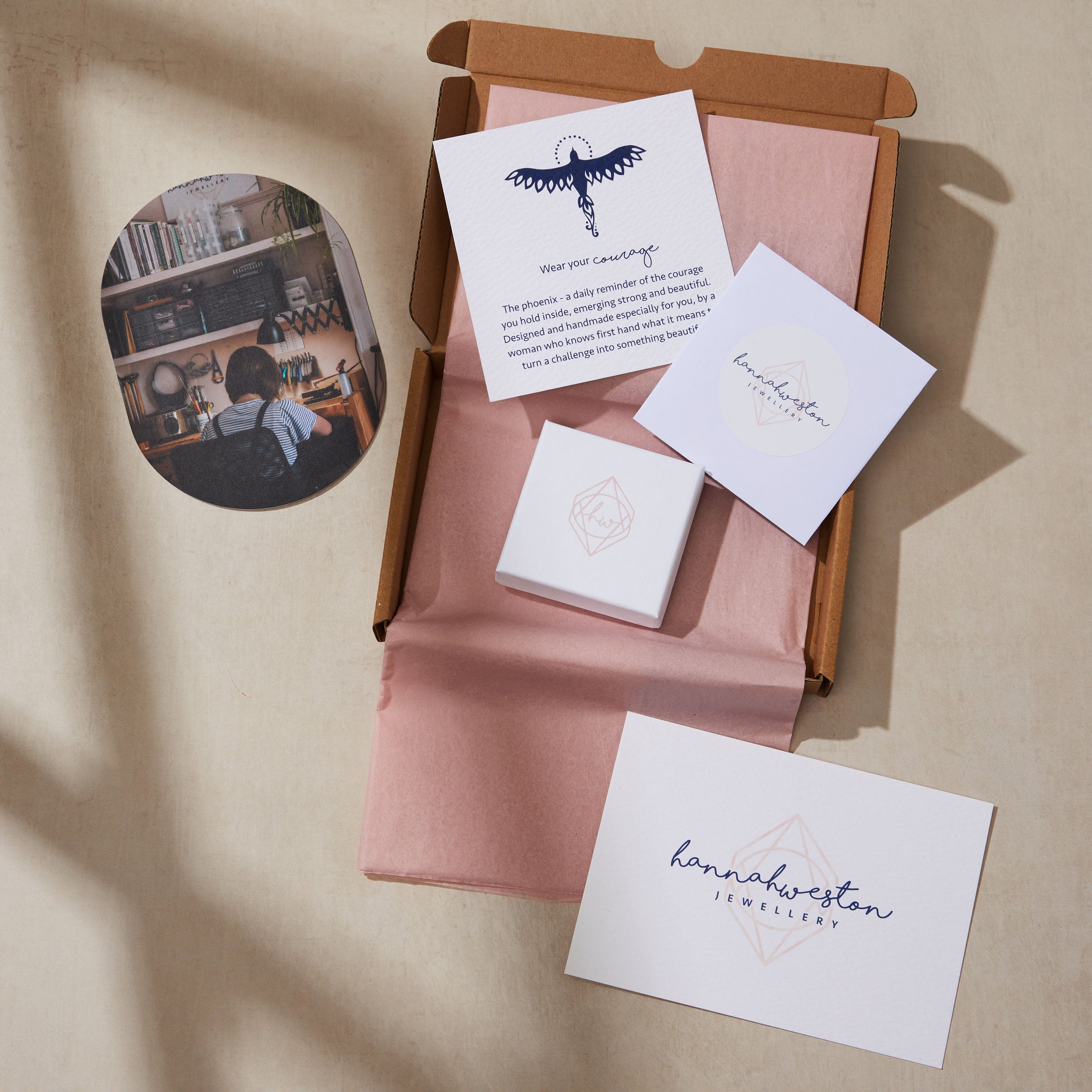Jewelry packaging with pink fabric, cards, and a small round mirror on a beige surface.