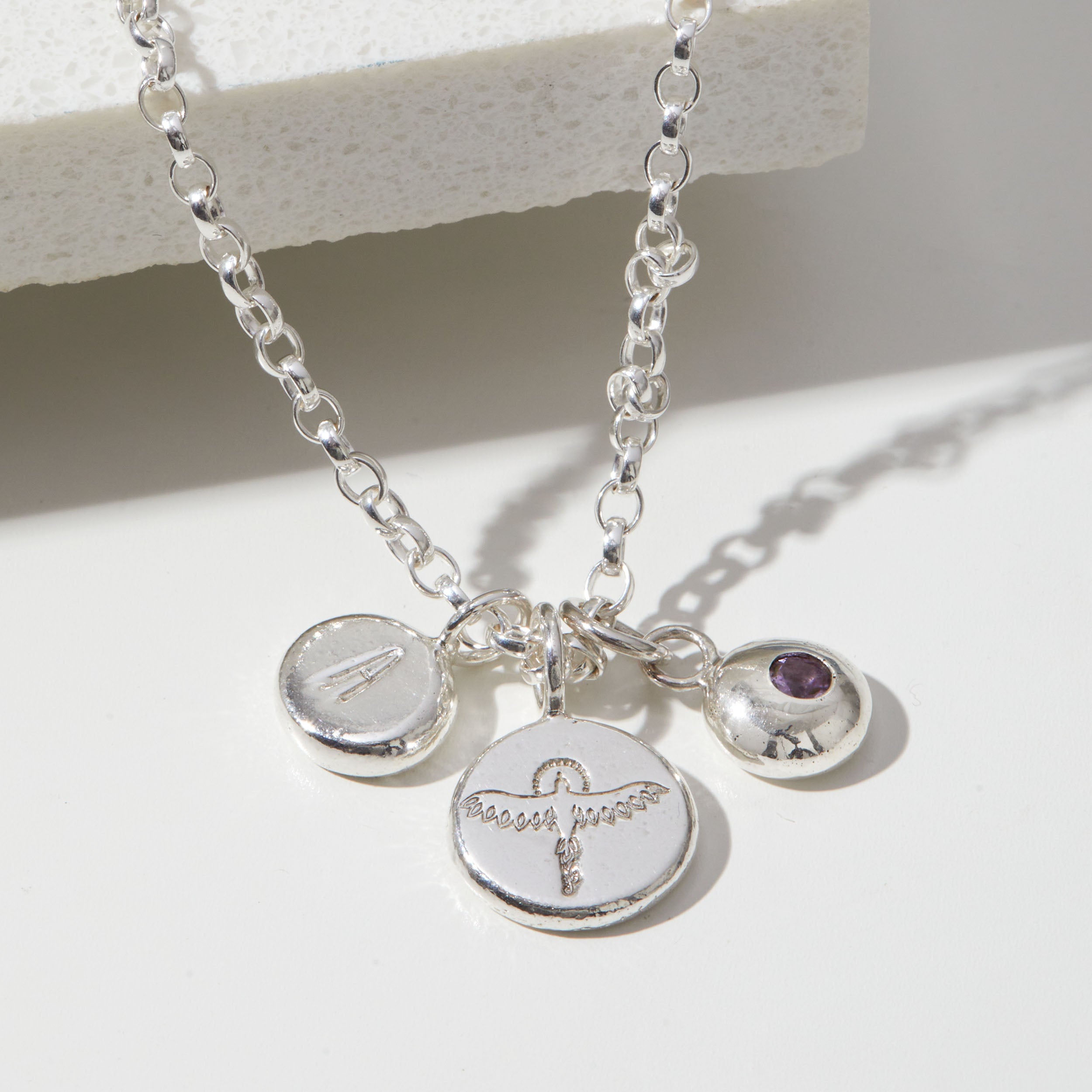 Silver necklace with initial, phoenix and birthstone charms on a white background