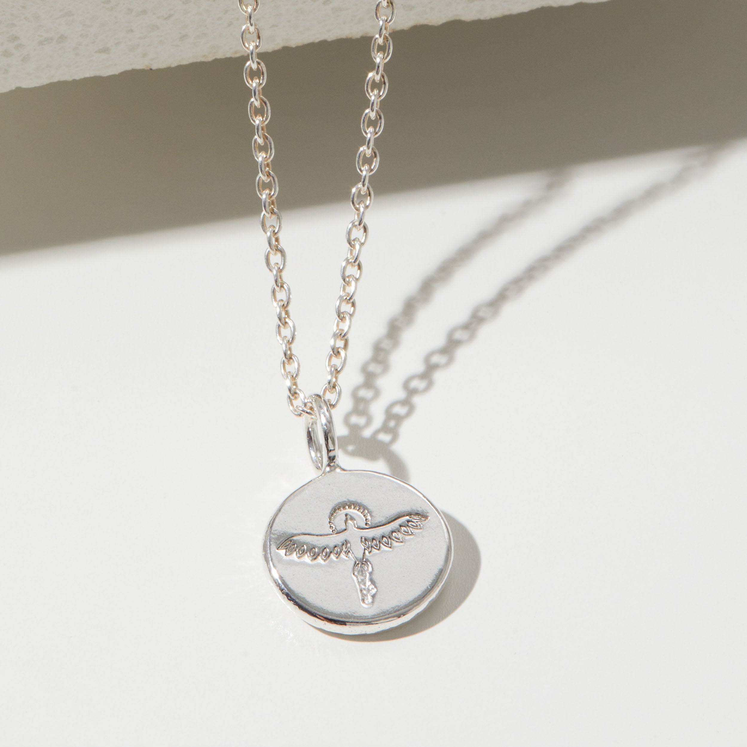 Silver phoenix necklace with a round pendant on a light background
