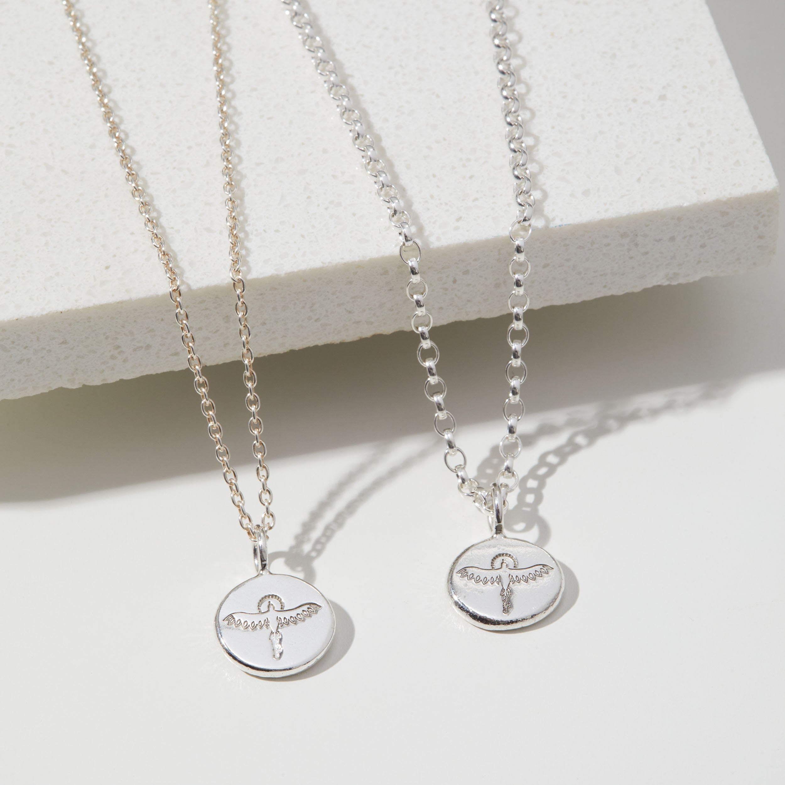 Two silver necklaces with stamped phoenix pendants on a white surface
