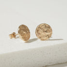 Gold round bark textured earrings on a light gray surface