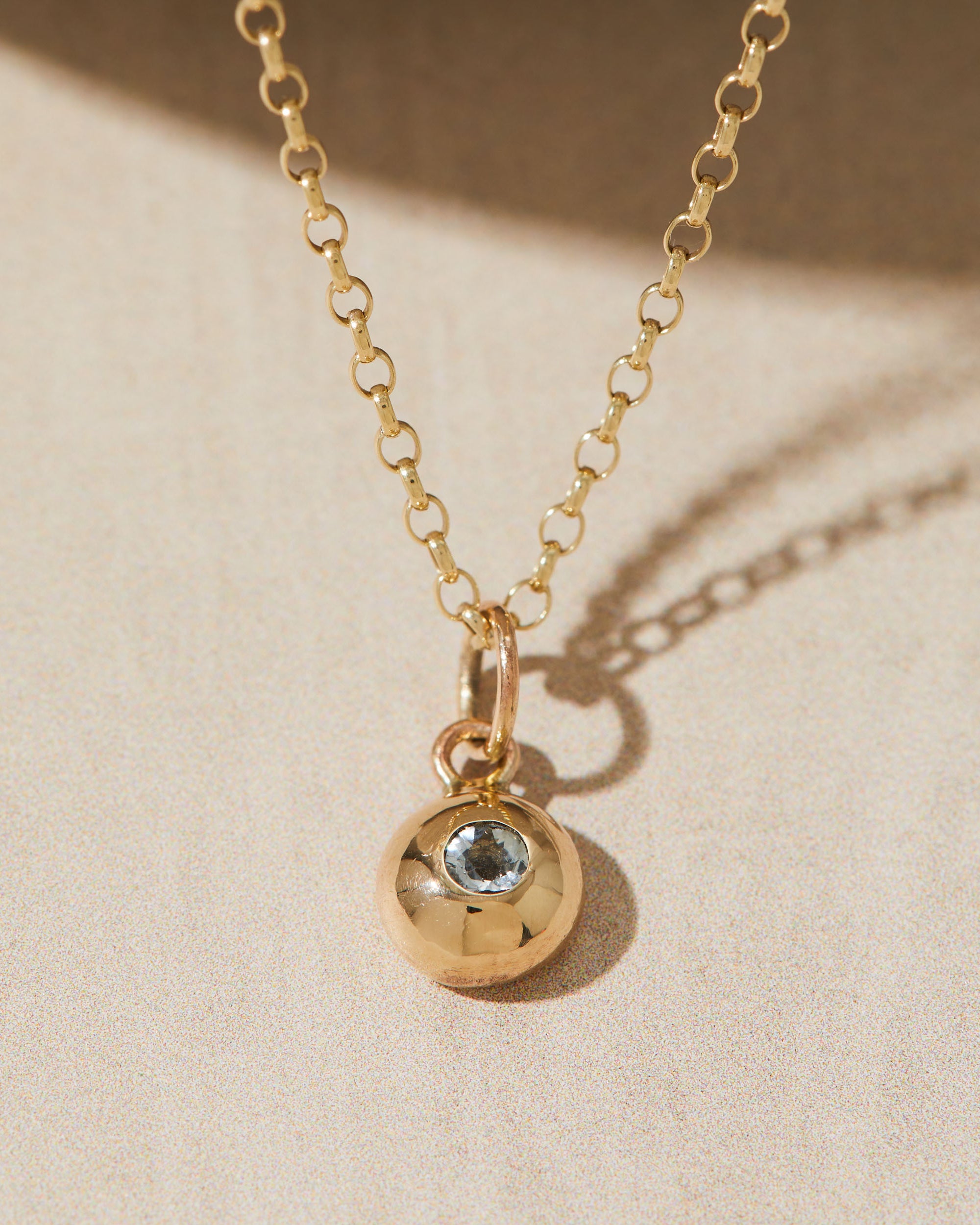 Gold necklace with a gemstone pendant featuring a gemstone on a beige background