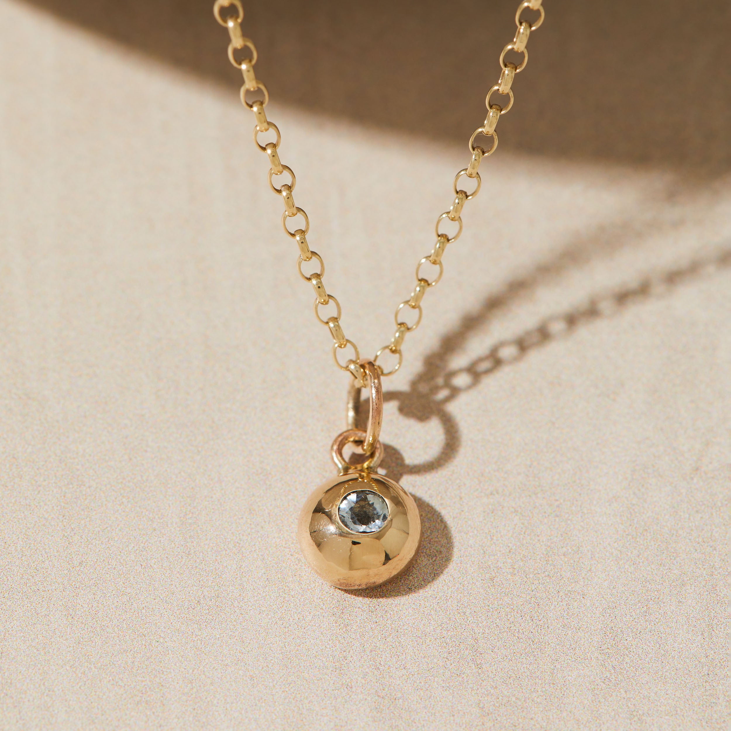 Gold necklace with a gemstone pendant featuring a gemstone on a beige background