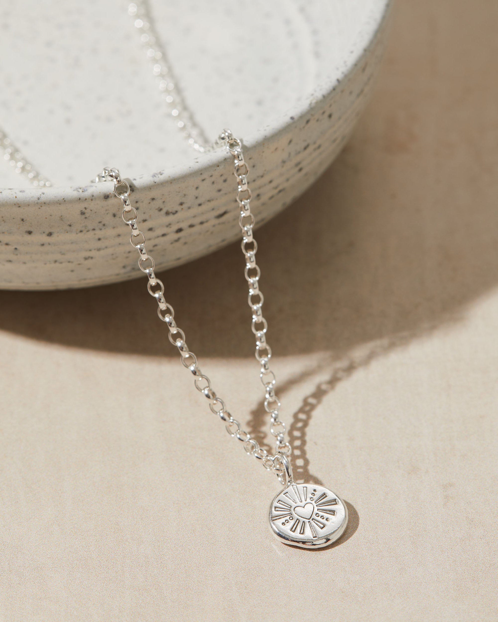 Silver necklace with a heart pendant on a beige surface