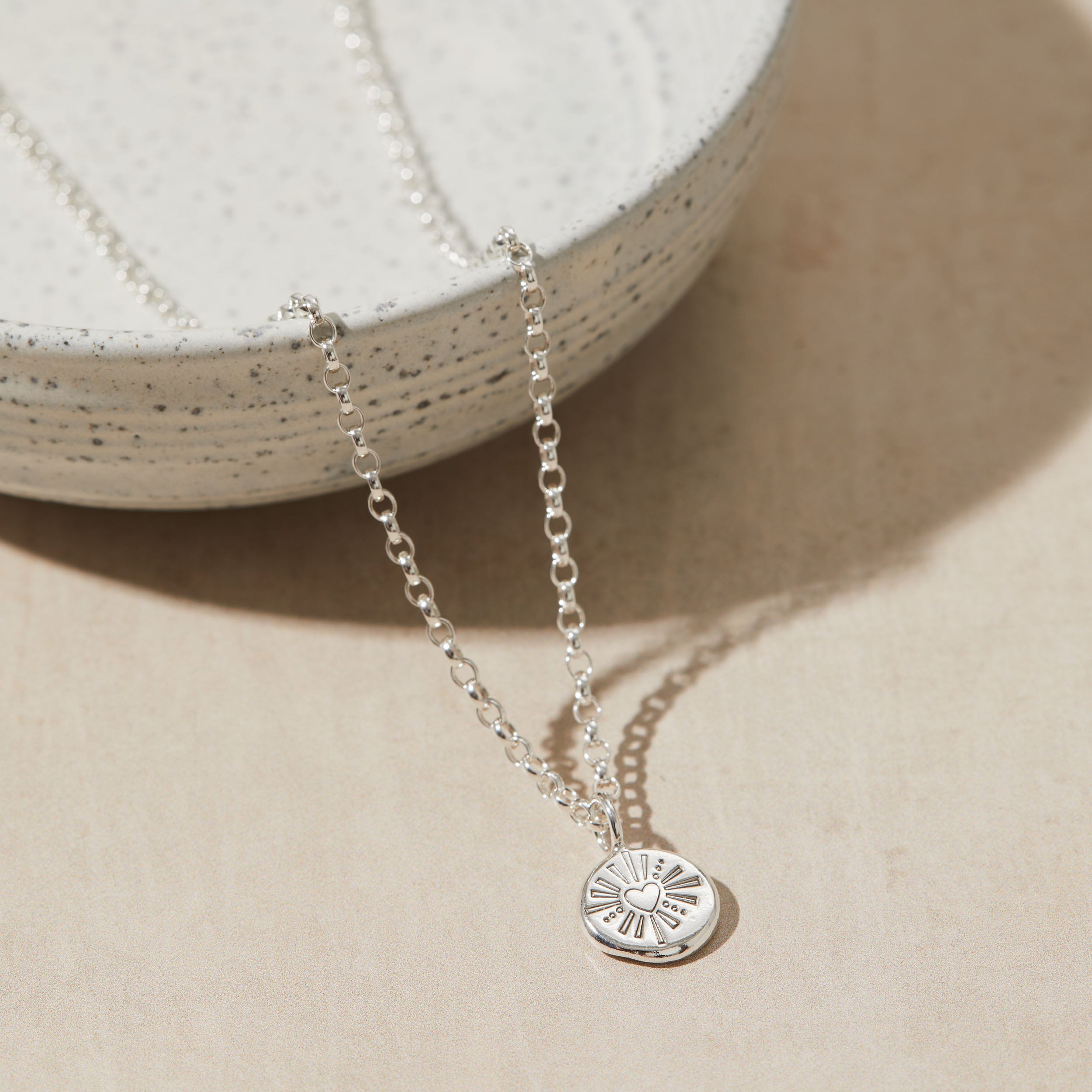 Silver necklace with a heart pendant on a beige surface