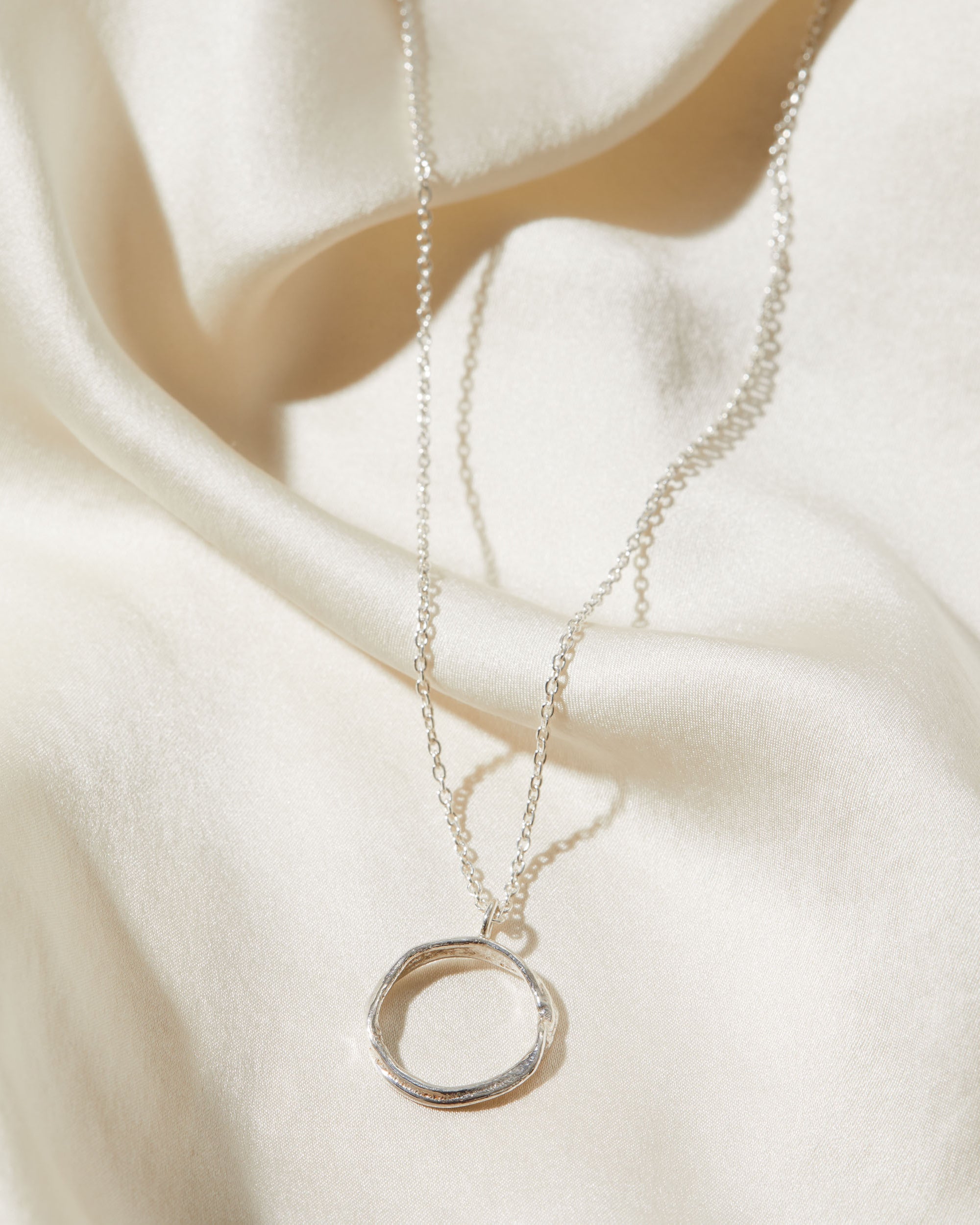 Silver necklace with a circular pendant on a white fabric background