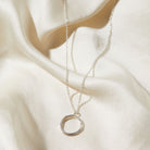 Silver necklace with a circular pendant on a white fabric background