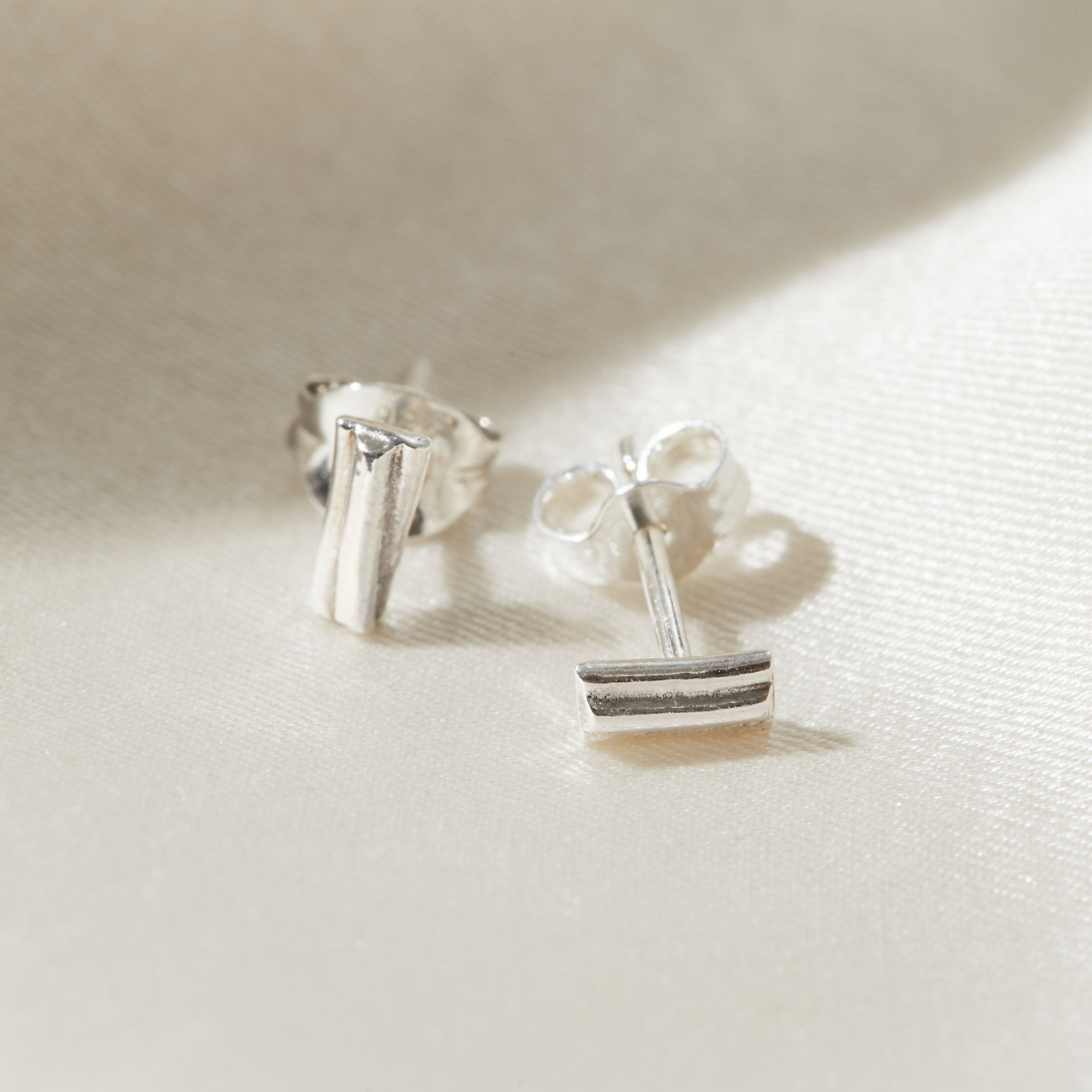 Silver stud earrings on a light fabric background