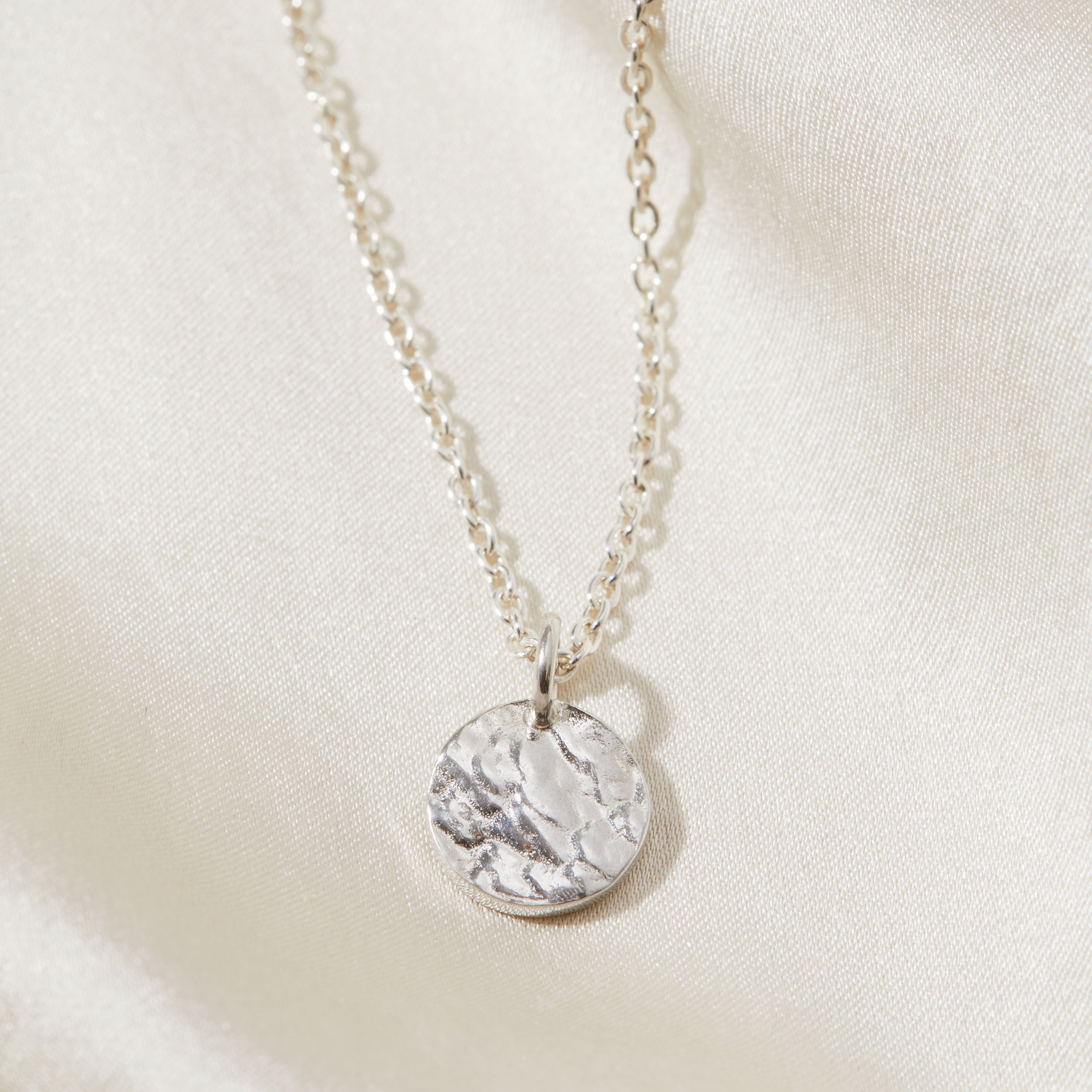 Silver necklace with a tree texture pendant on a light beige background