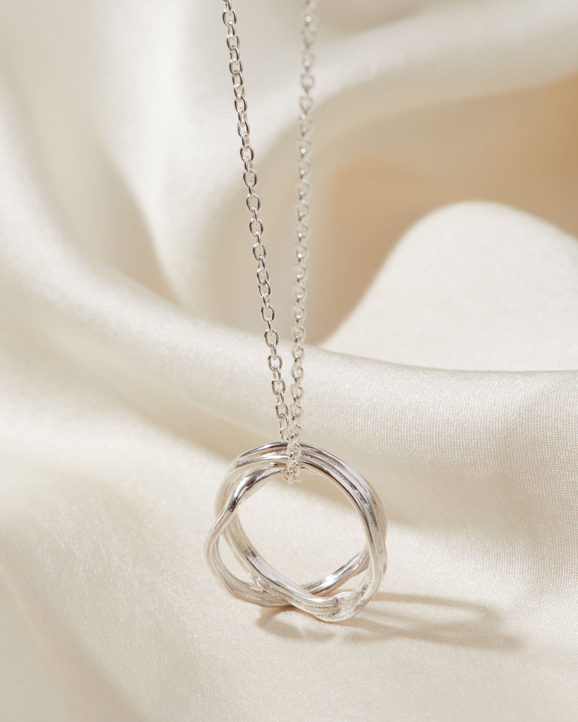 Silver necklace with a unique ring pendant on a soft beige fabric background