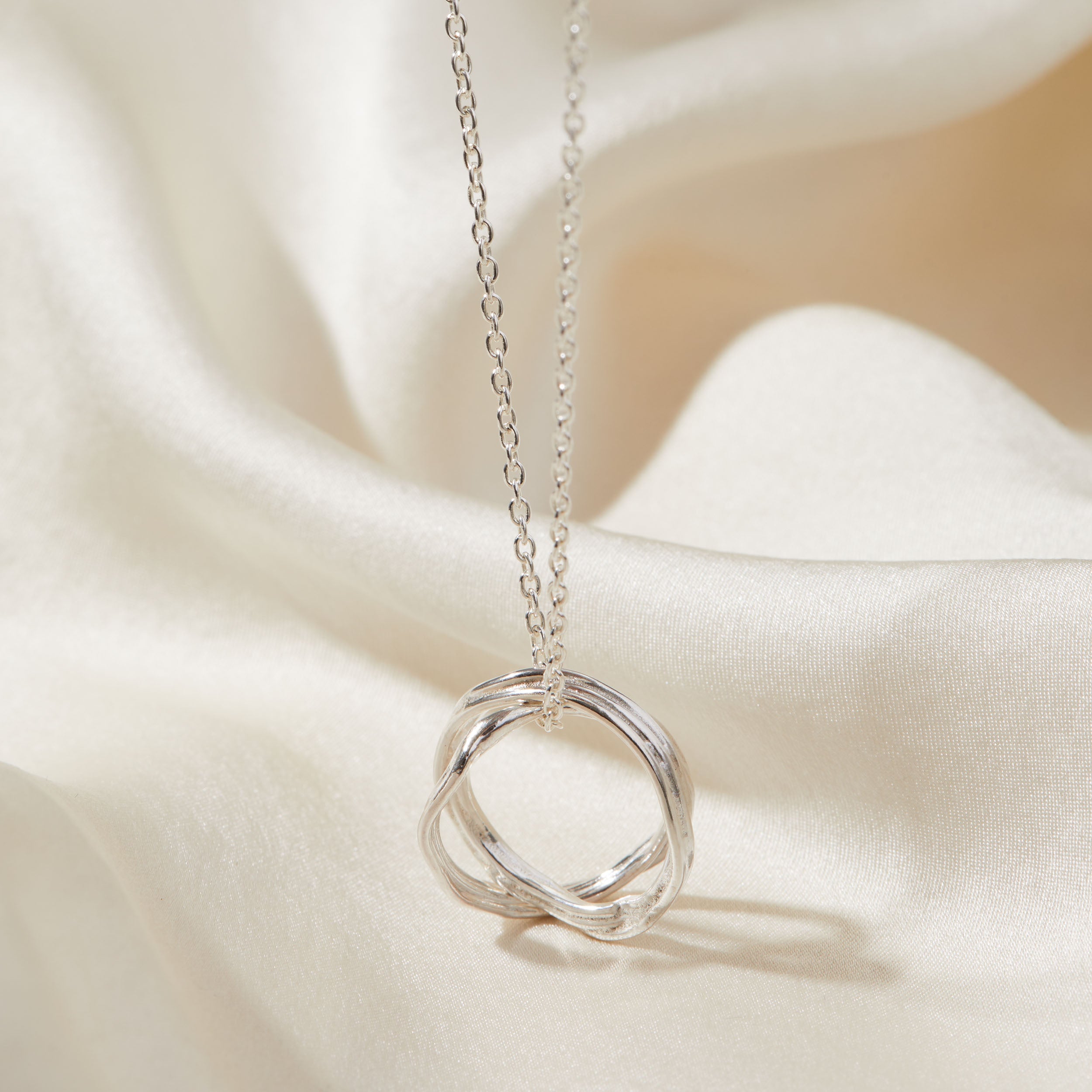 Silver necklace with a unique ring pendant on a soft beige fabric background