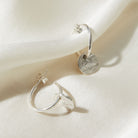 Pair of silver hoop earrings with bark charms on a light fabric background