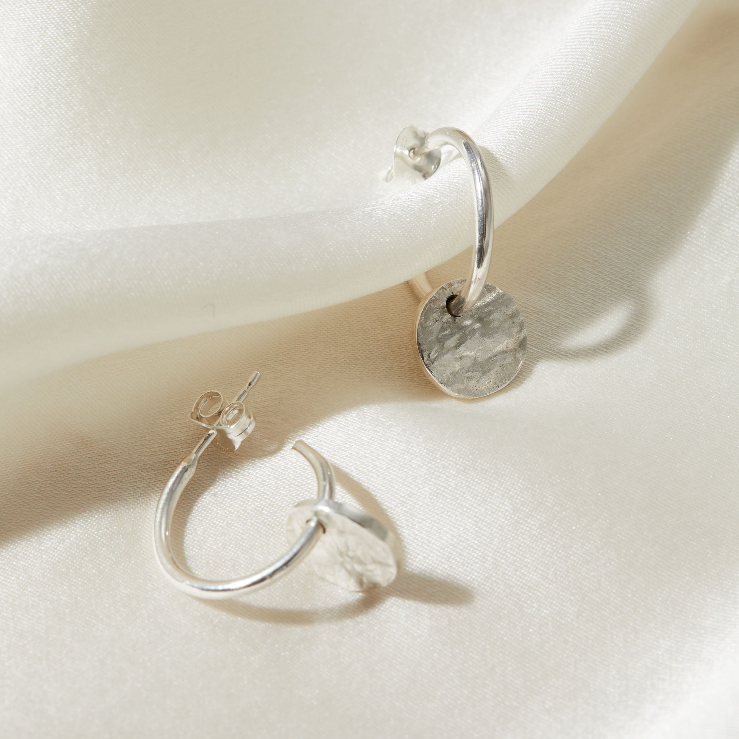 Pair of silver hoop earrings with bark charms on a light fabric background