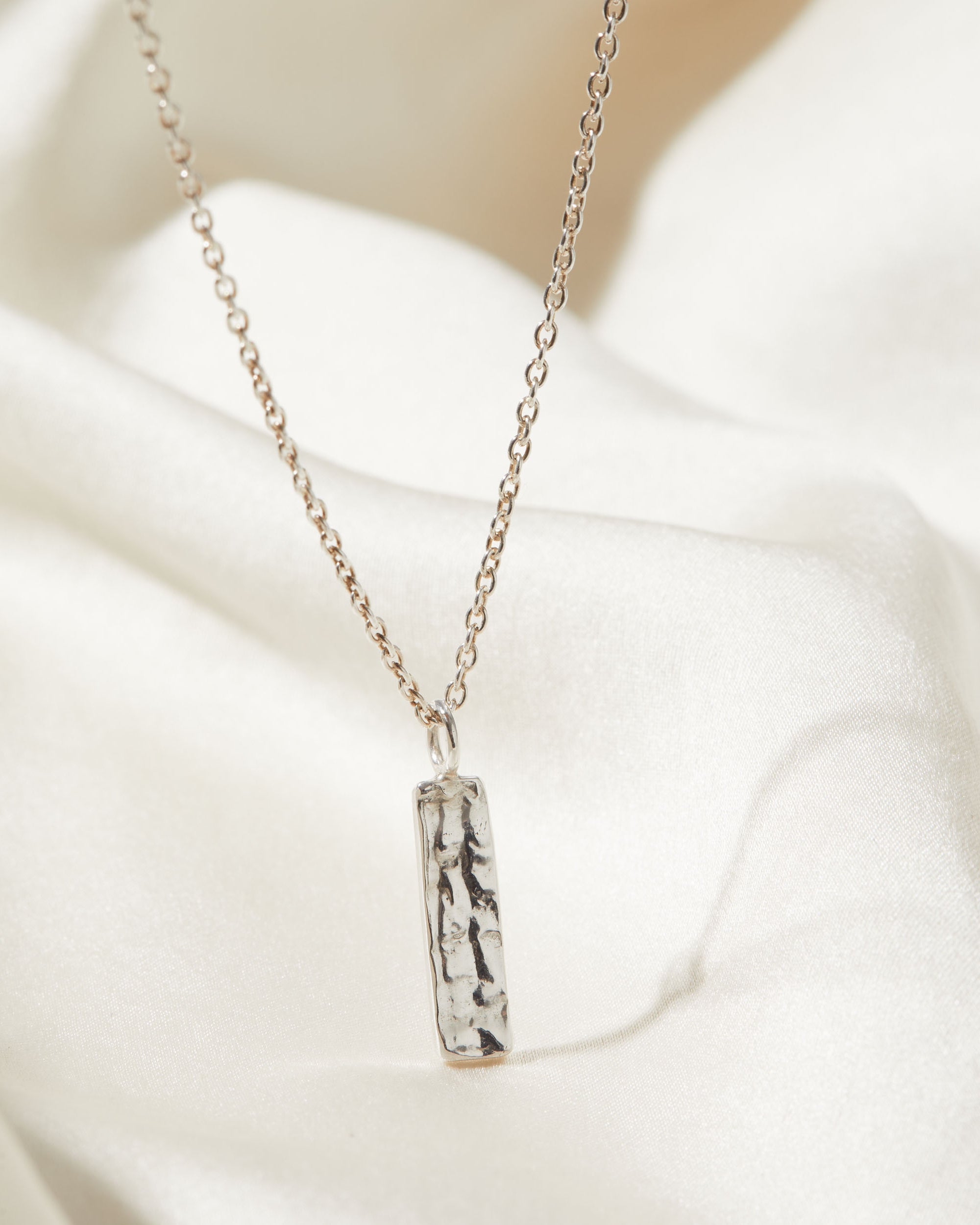 Silver necklace with a bark texture pendant on a white fabric background