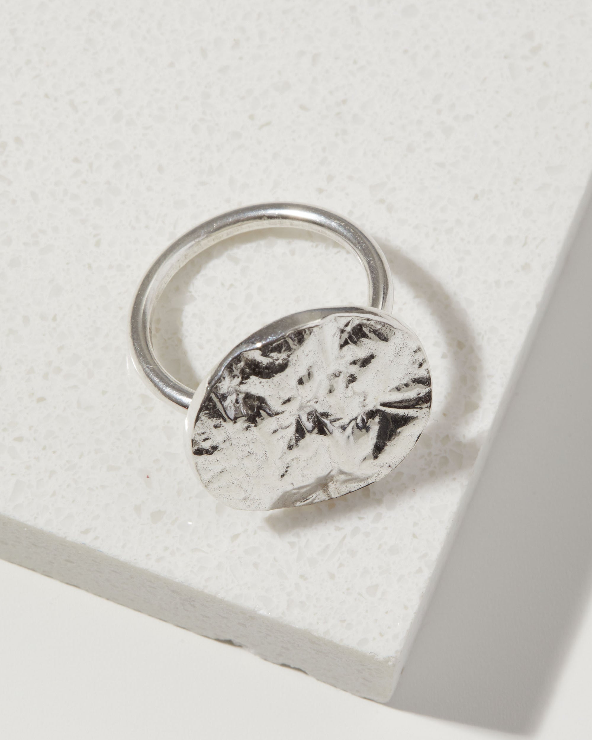 Silver ring with a bark textured circular design on a light gray background