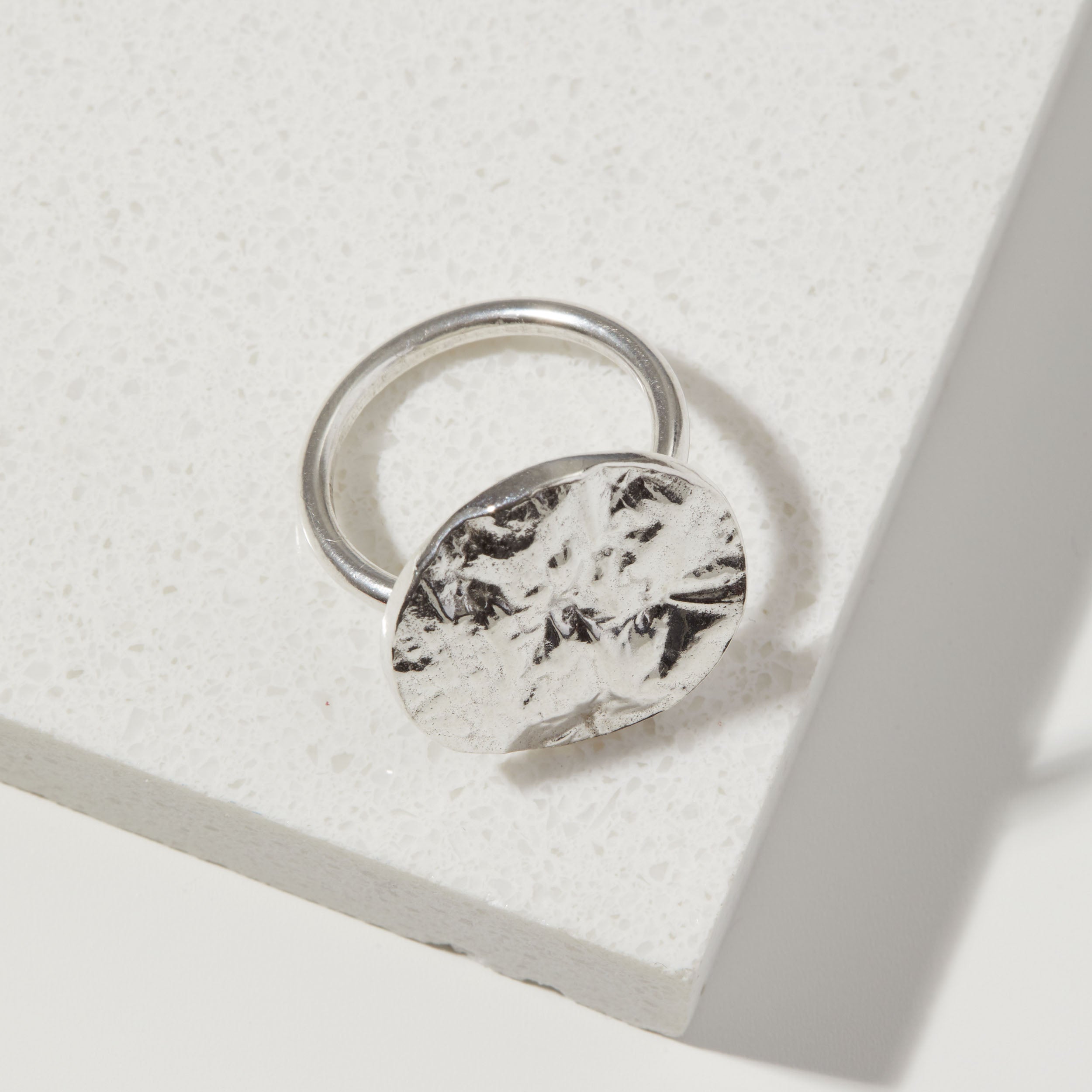 Silver ring with a bark textured circular design on a light gray background