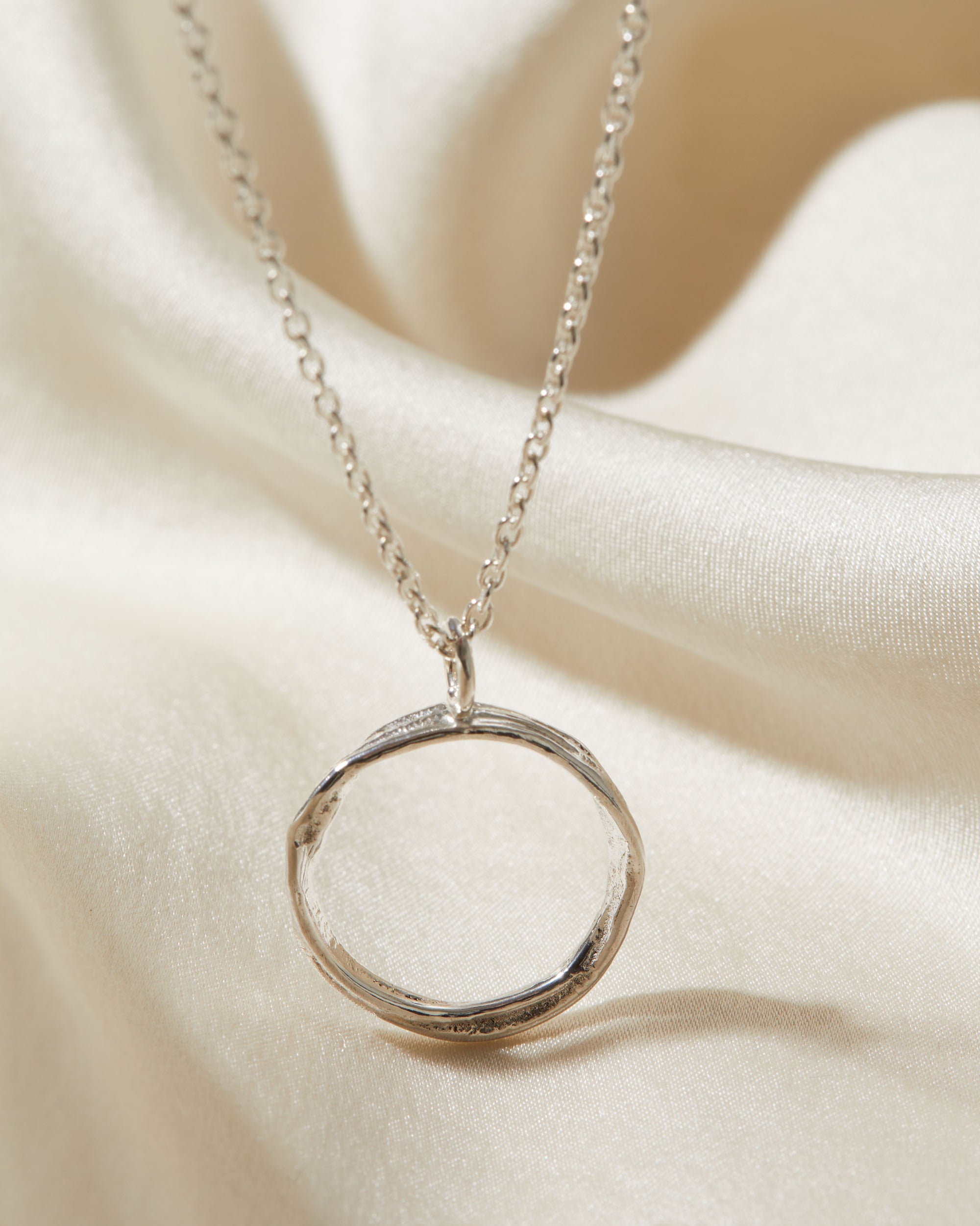 Silver necklace with a circular pendant on a beige fabric background