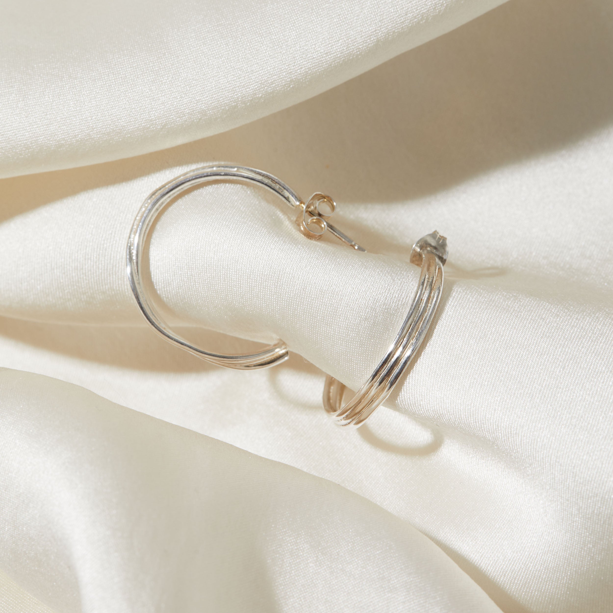 Silver hoop earrings on a white fabric background