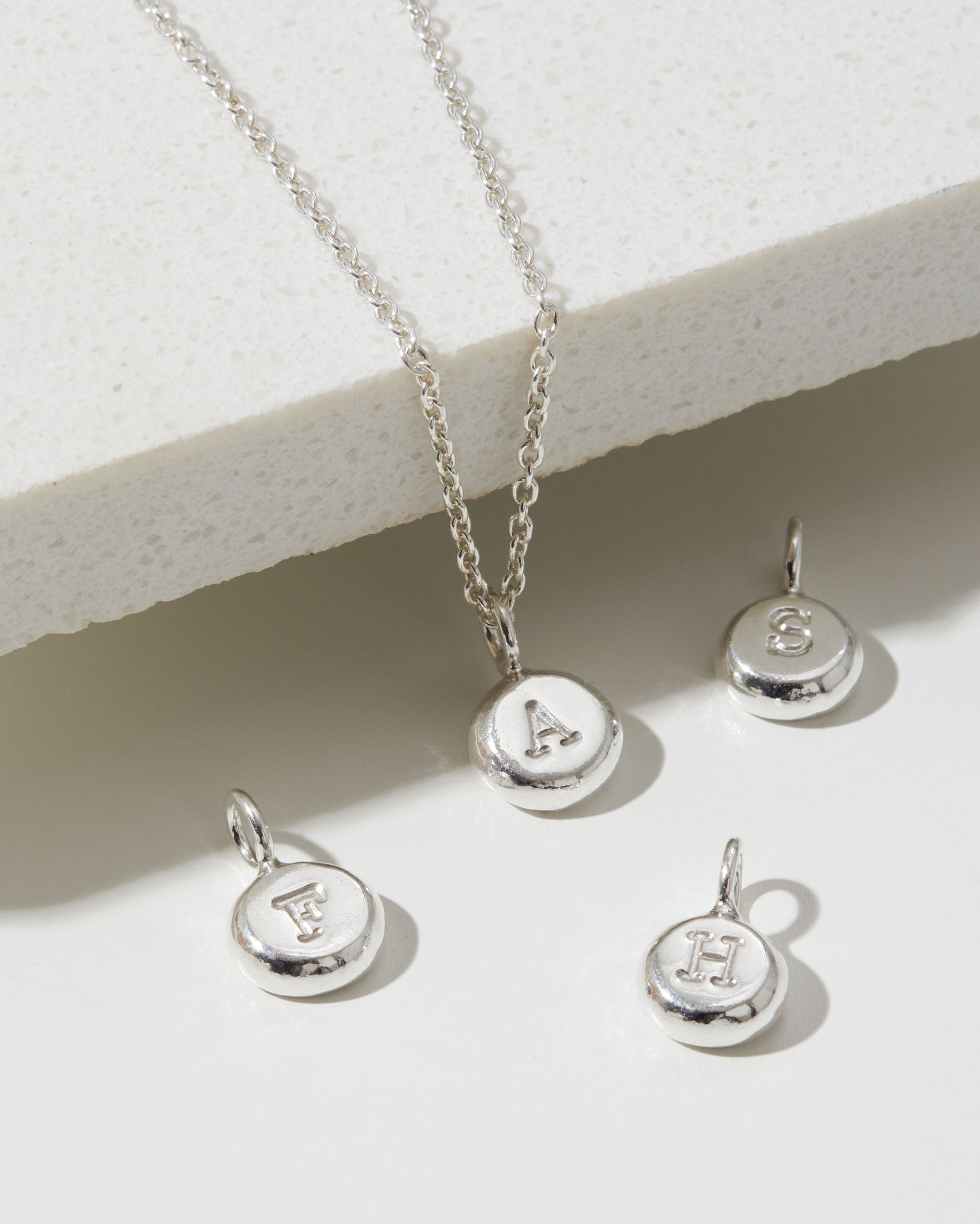 Silver necklace with letter pendants on a light background