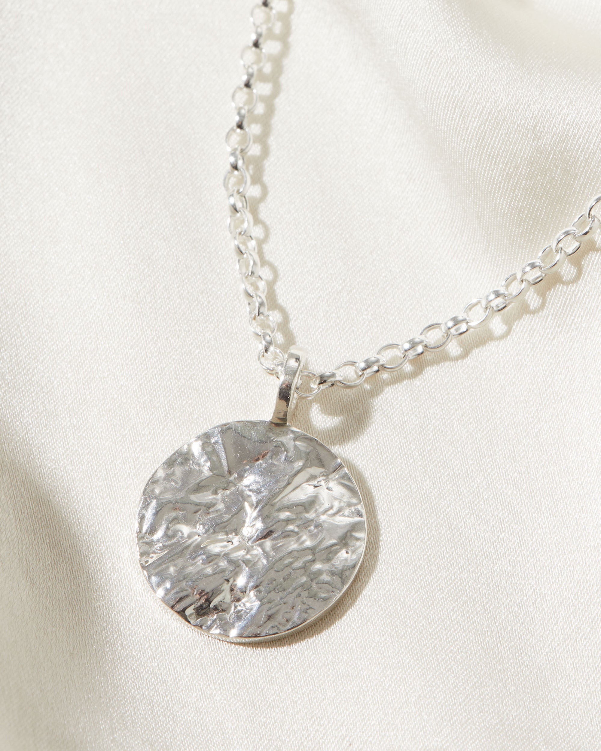 Silver necklace with a statement bark textured pendant on a light background