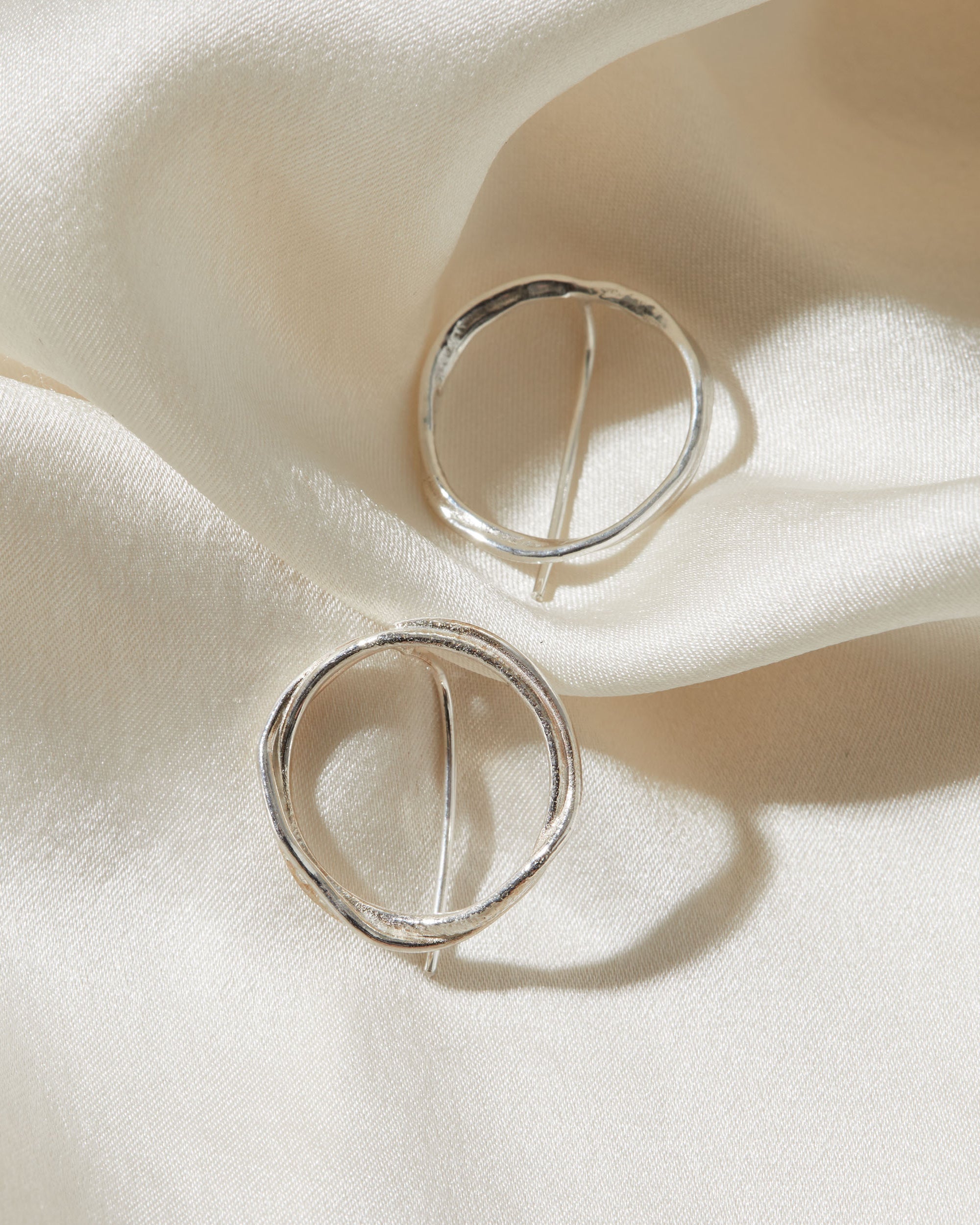 Silver circular earrings on a soft white fabric background