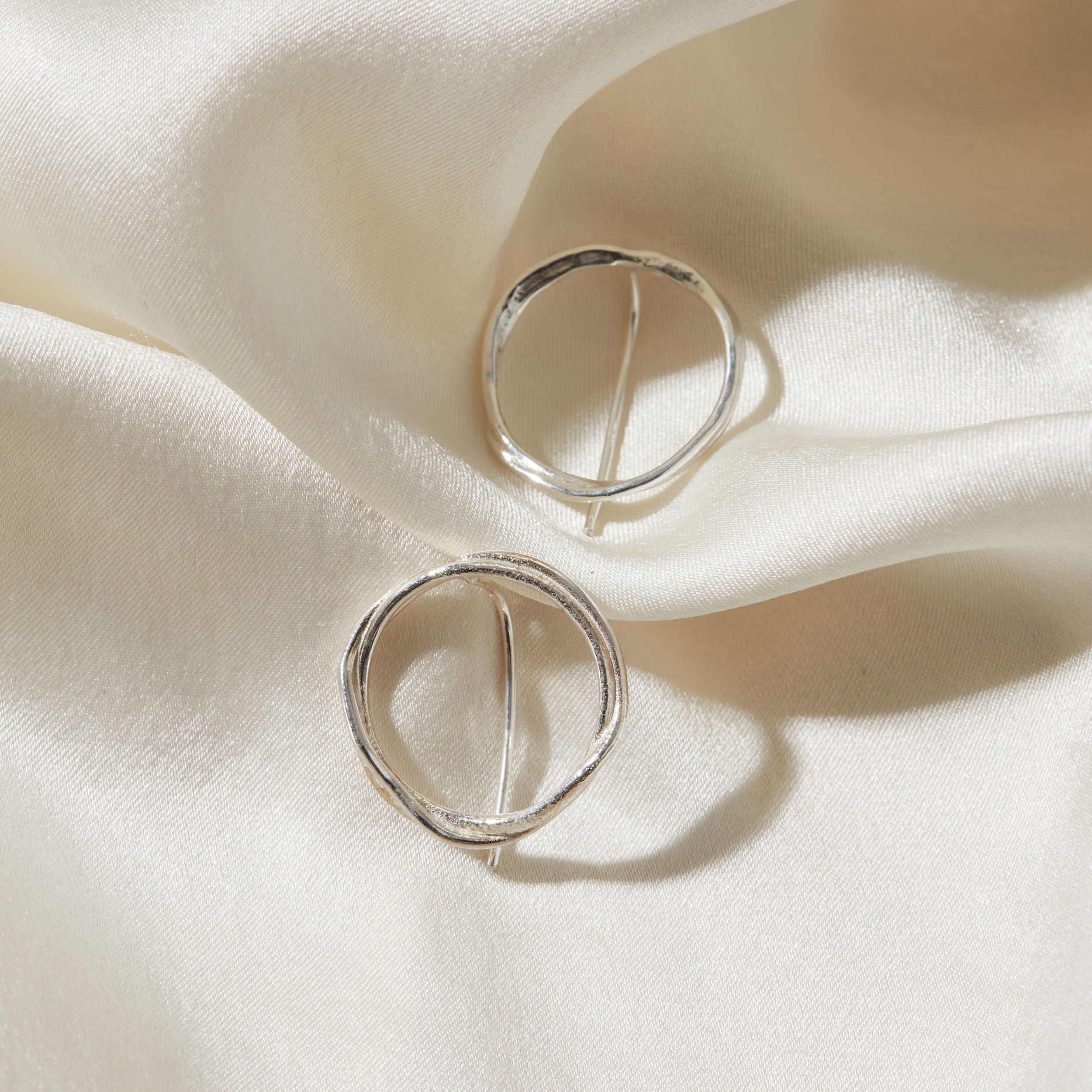 Silver circular earrings on a soft white fabric background