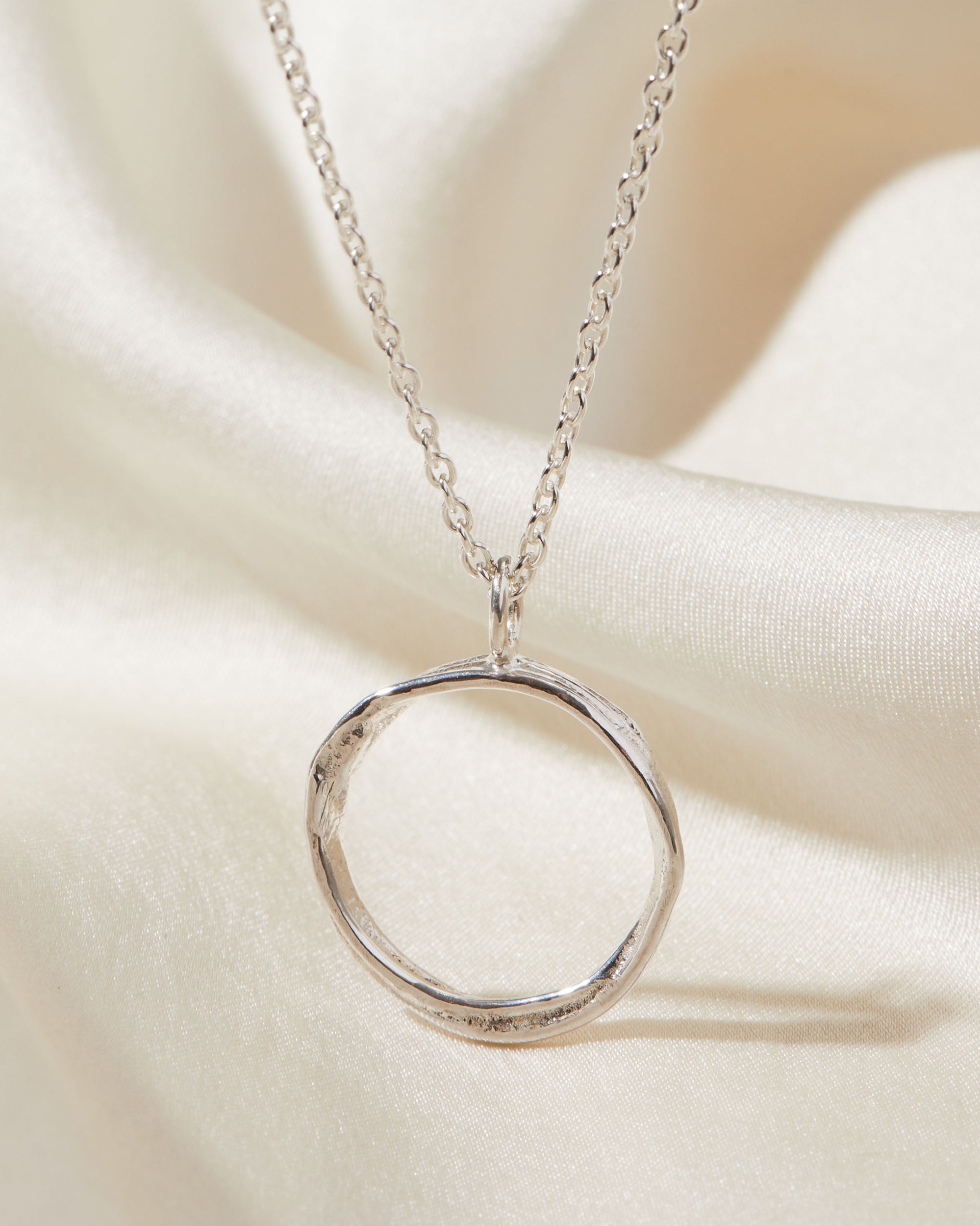 Silver circular pendant necklace on a soft beige fabric background