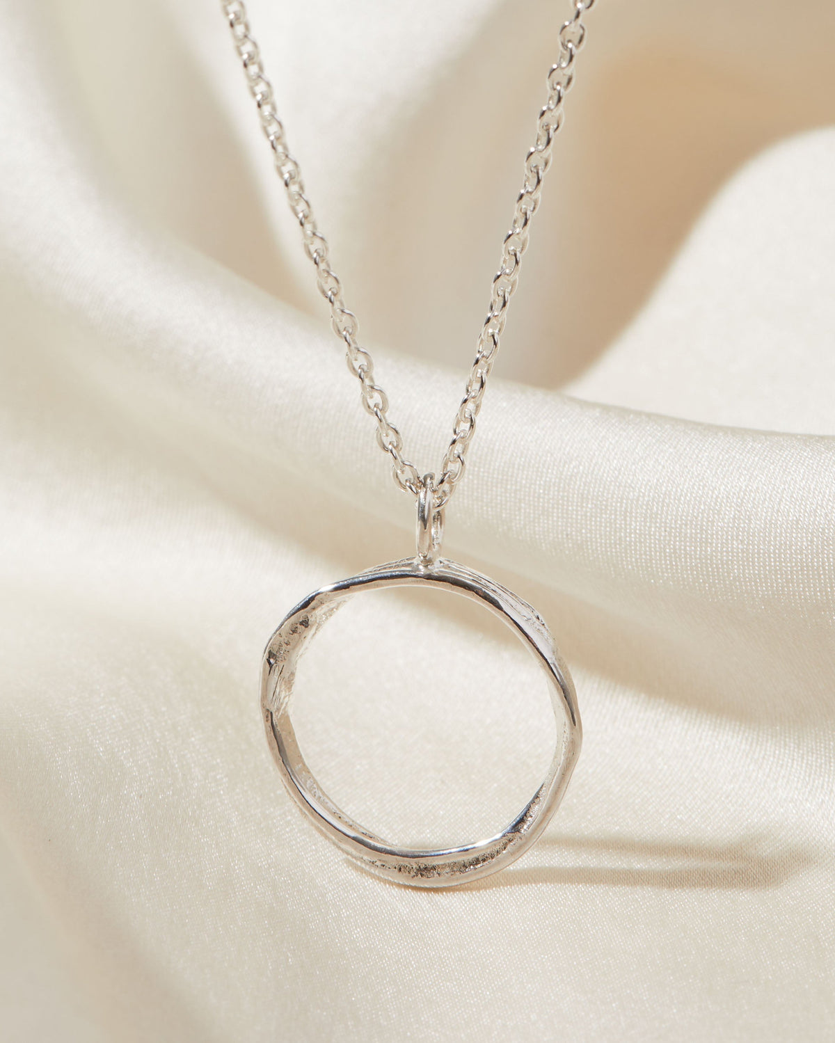 Silver circular pendant necklace on a soft beige fabric background