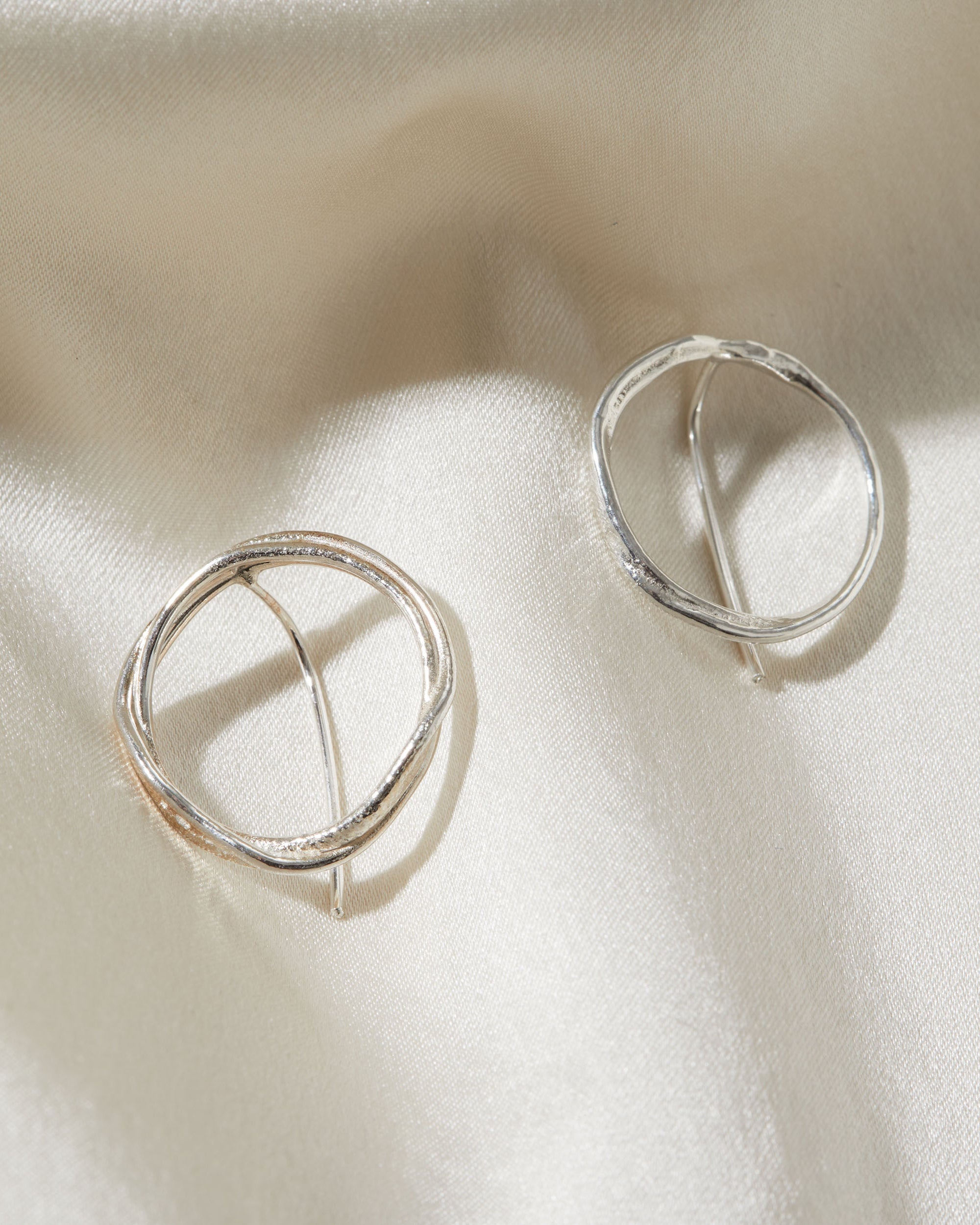 Pair of circular silver earrings on a light fabric background