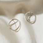Pair of circular silver earrings on a light fabric background
