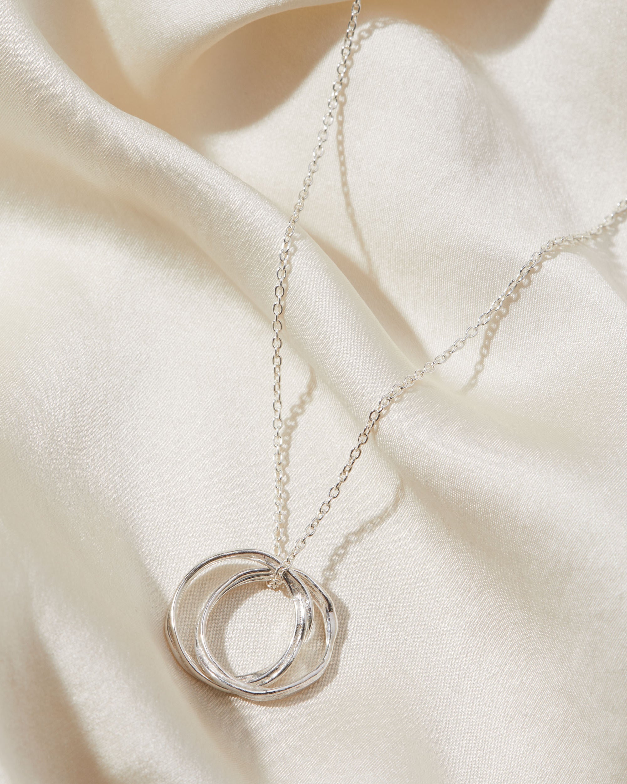 Silver necklace with a double-circle pendant on a beige fabric background