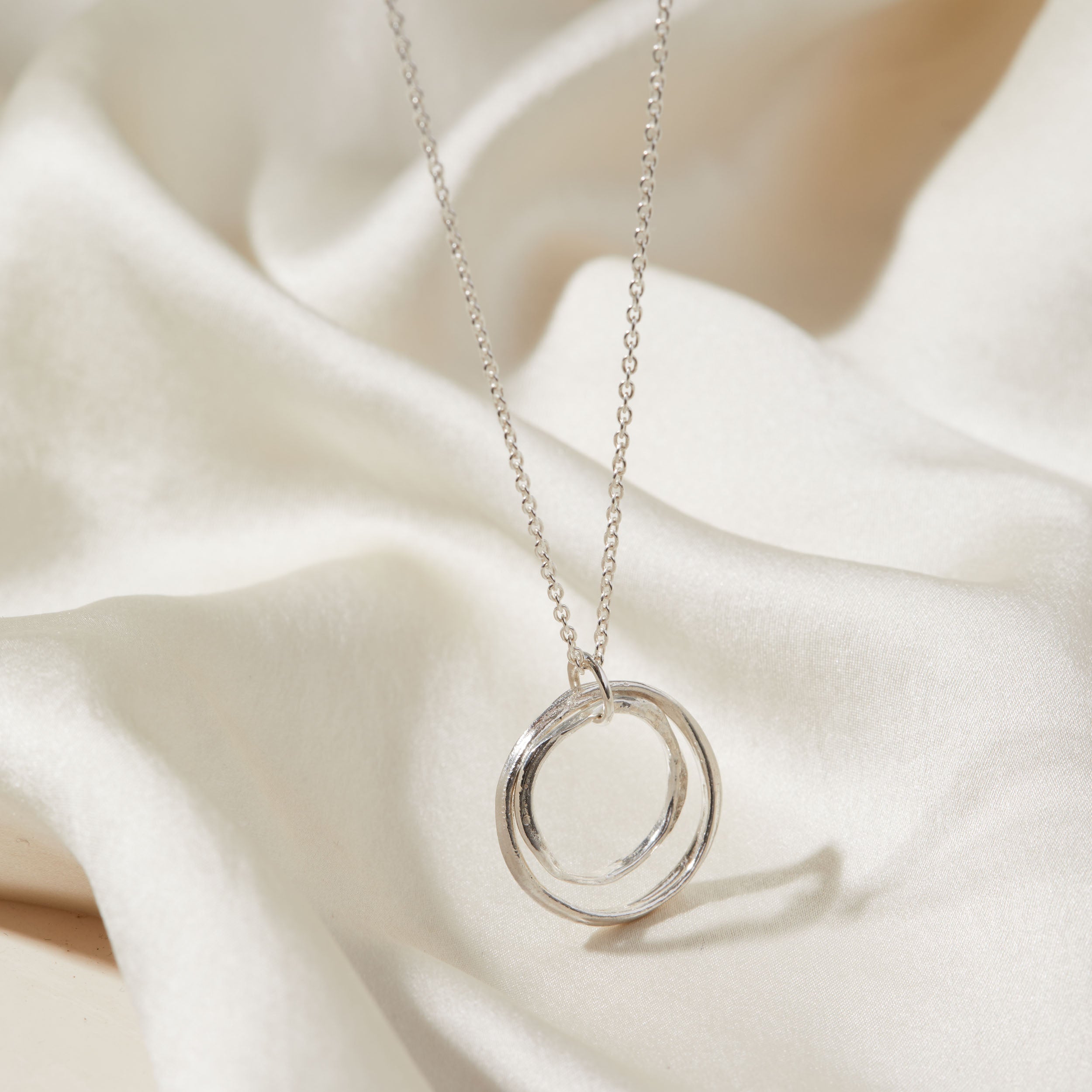 Silver necklace with a double-circle pendant on a white fabric background