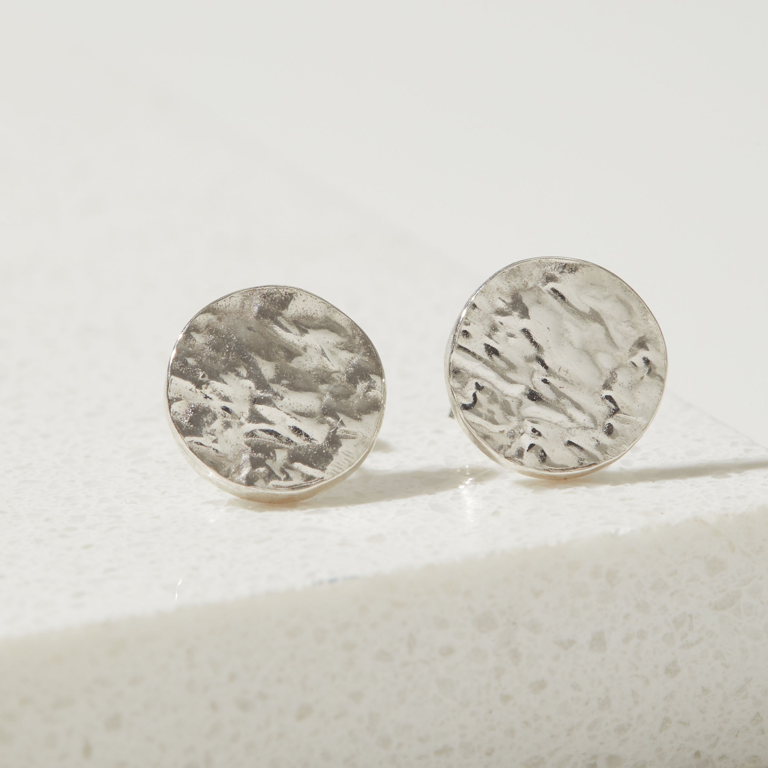 Pair of silver bark textured round earrings on a light background