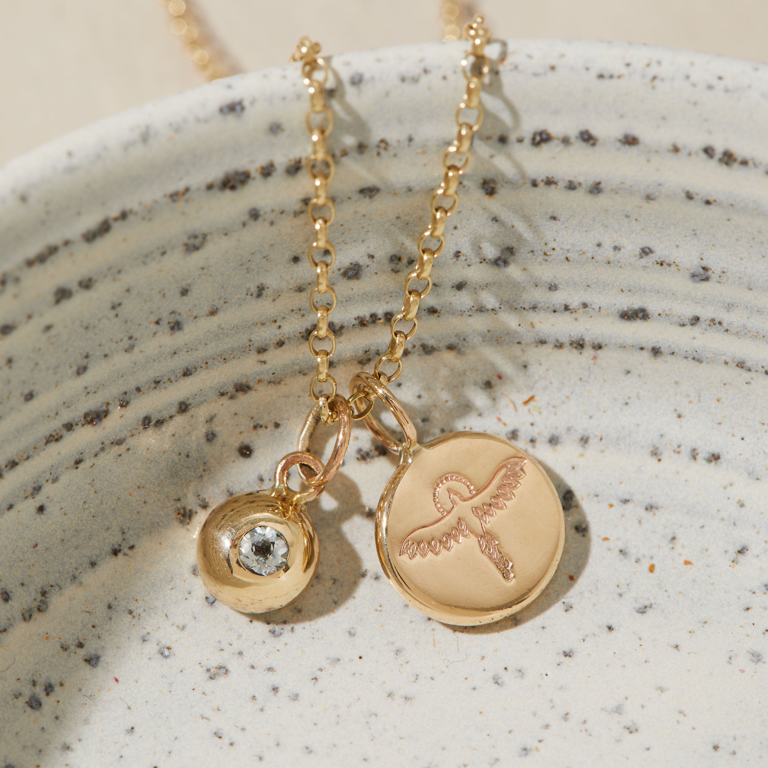 Gold necklace with phoenix and birthstone charms on a textured ceramic surface