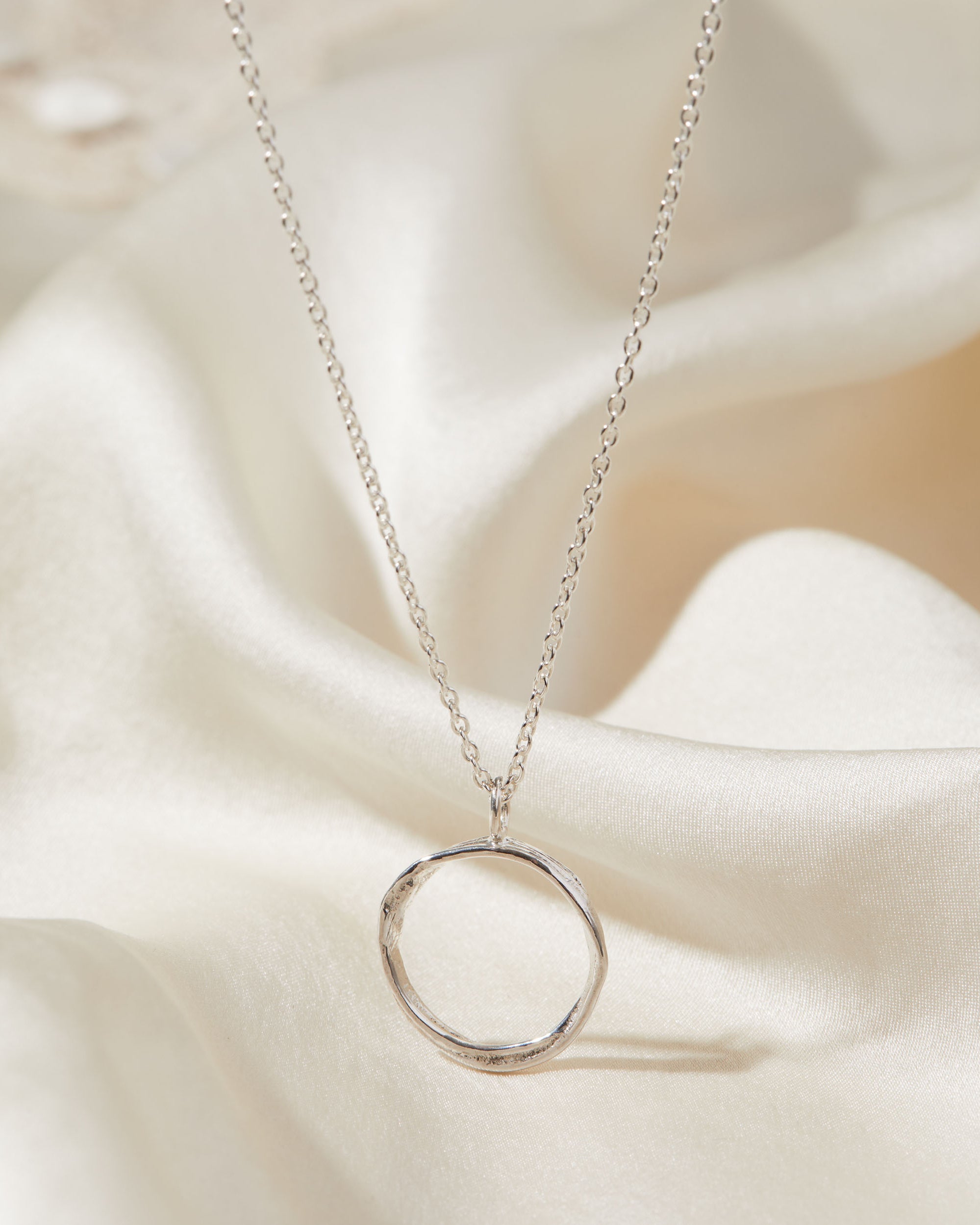 Silver necklace with a circular pendant on a soft fabric background