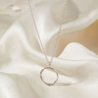 Silver necklace with a circular pendant on a soft fabric background