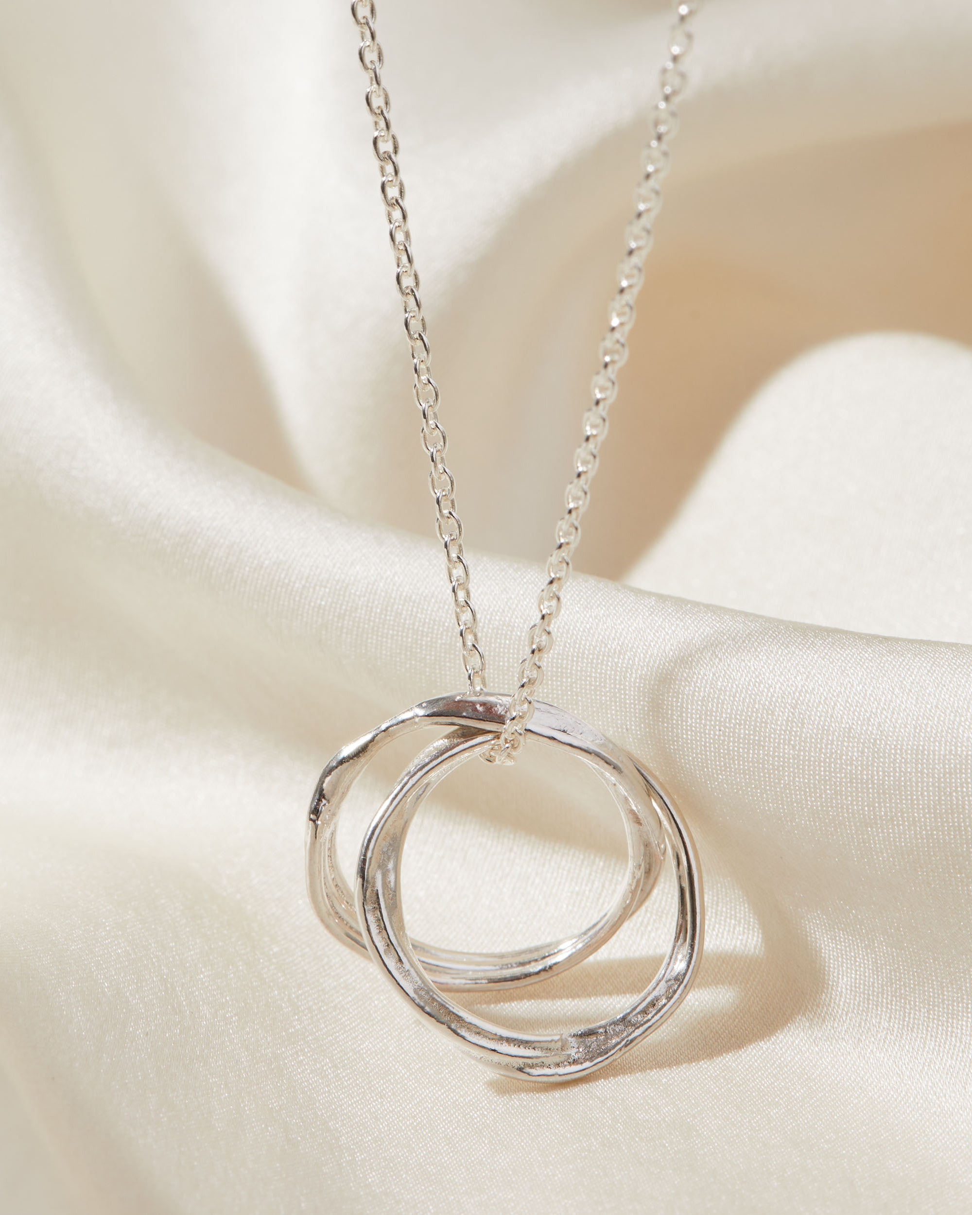 Silver necklace with a double ring pendant on a white fabric background