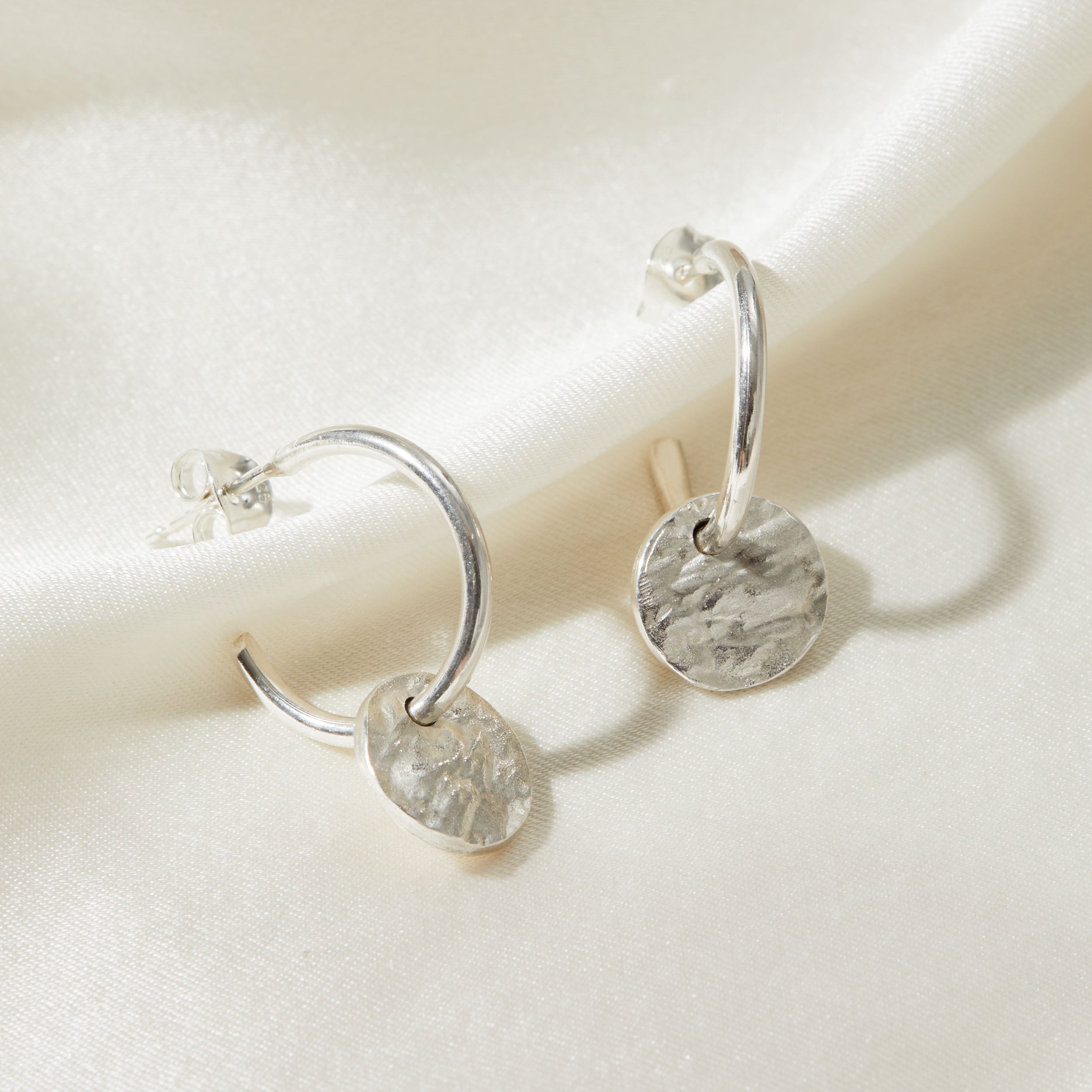 Silver hoop earrings with round bark textured pendants on a light background