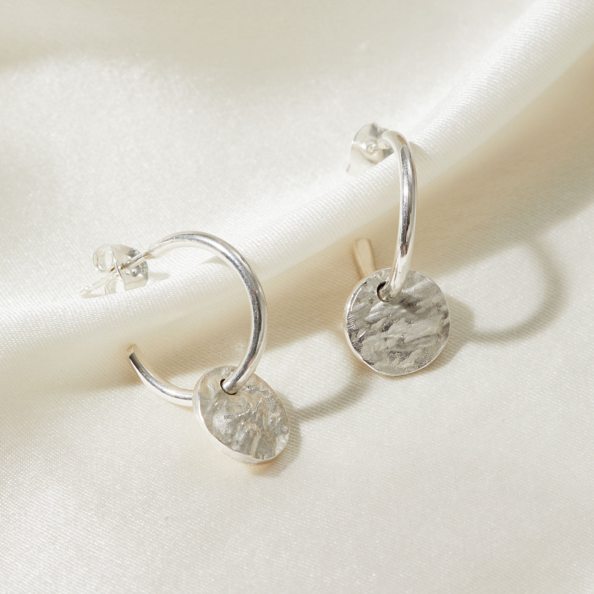 Silver hoop earrings with round bark textured pendants on a light background