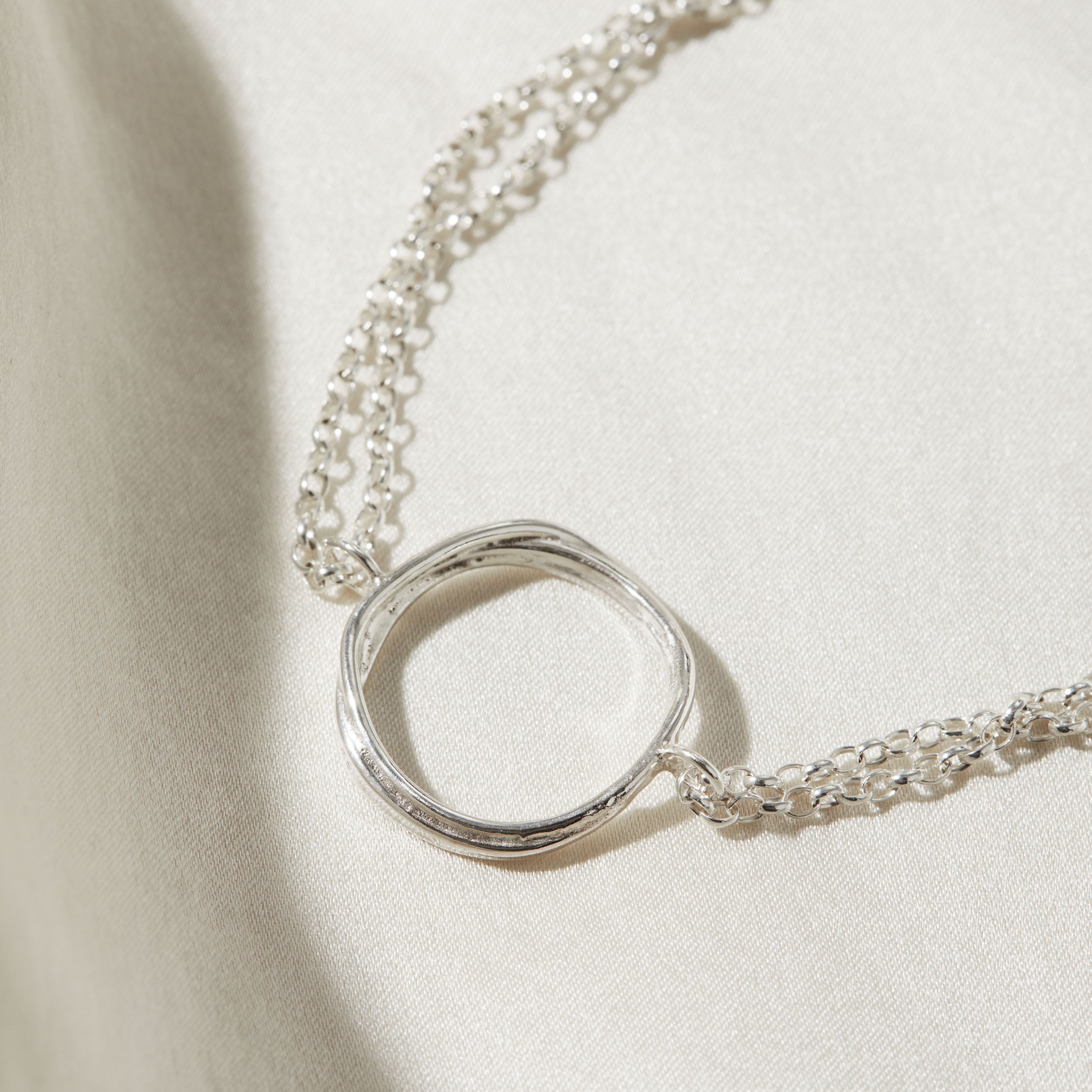 Silver necklace with a unique circular pendant on a beige background
