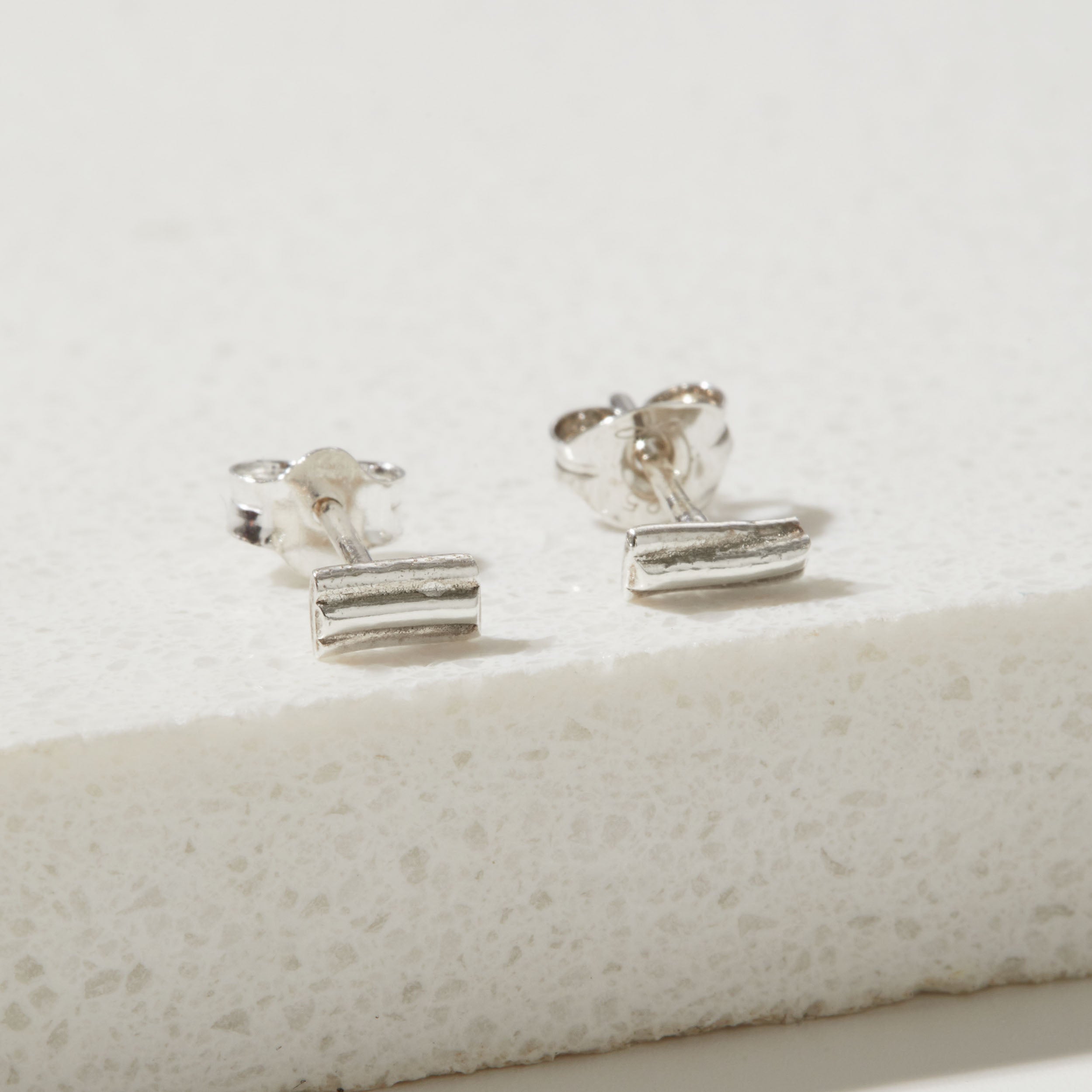 Pair of silver ripple stud earrings on a textured white surface