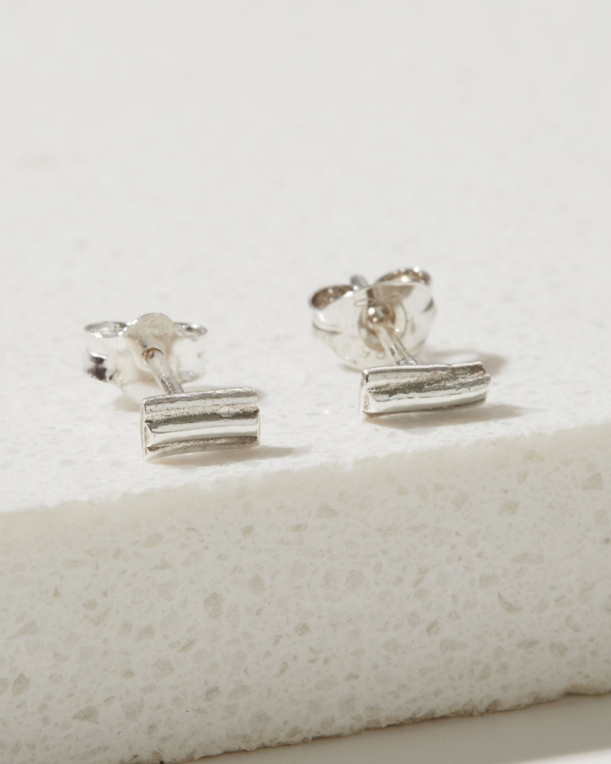 Pair of silver ripple stud earrings on a textured white surface